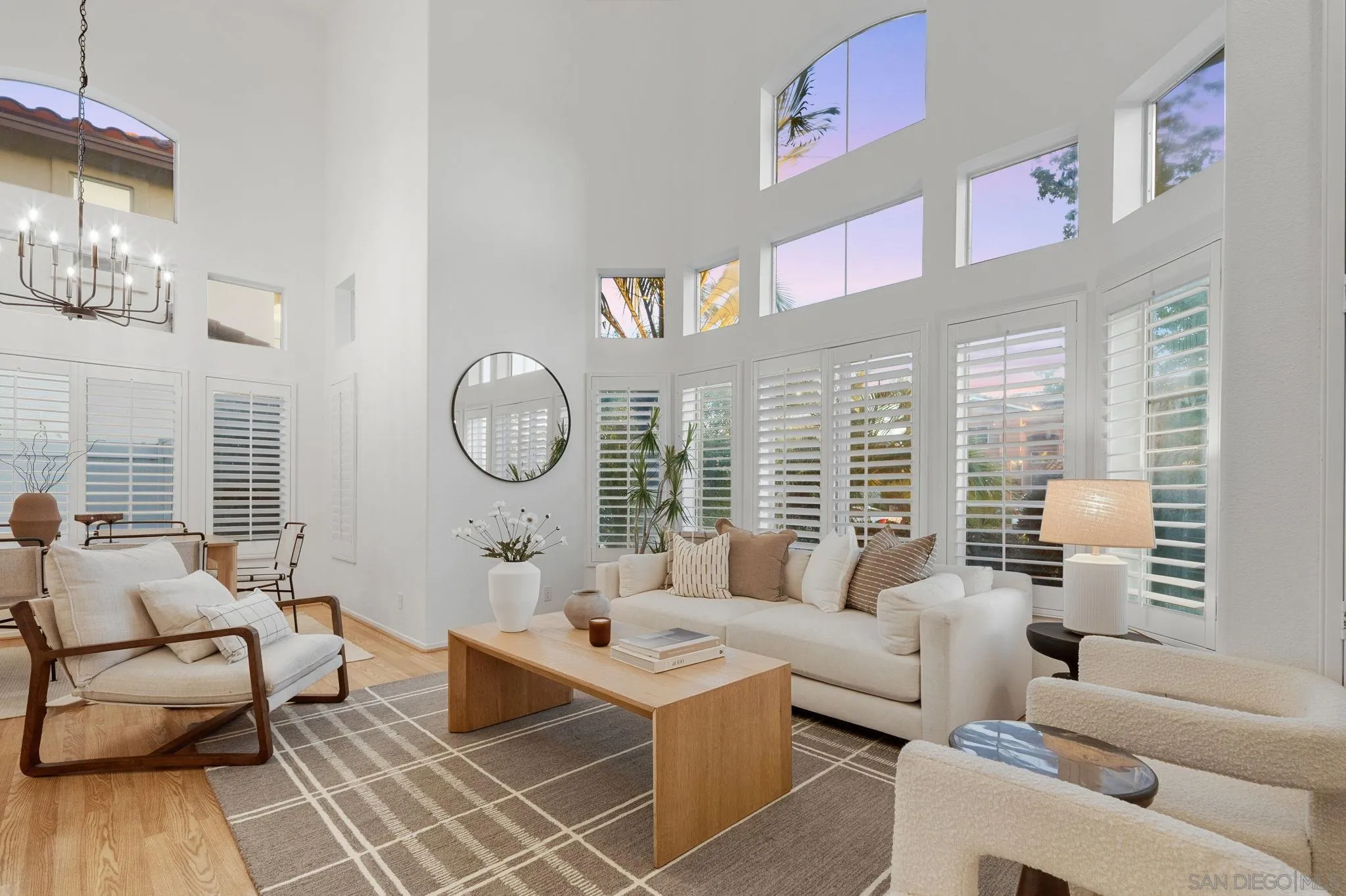 Double-height living room with white sofas, plantation shutters, and tall clerestory windows.