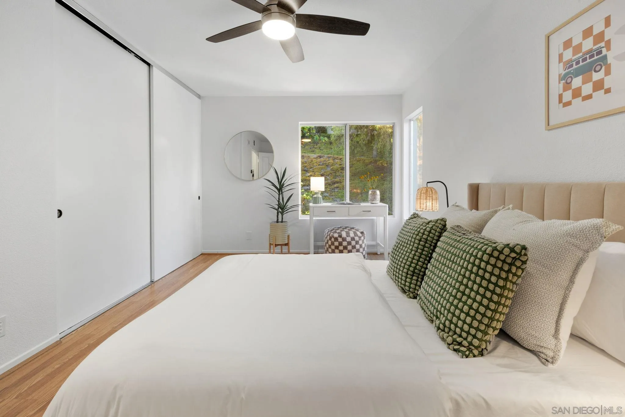 Furnished bedroom with green accent pillows, sliding closet doors, and a window overlooking greenery.