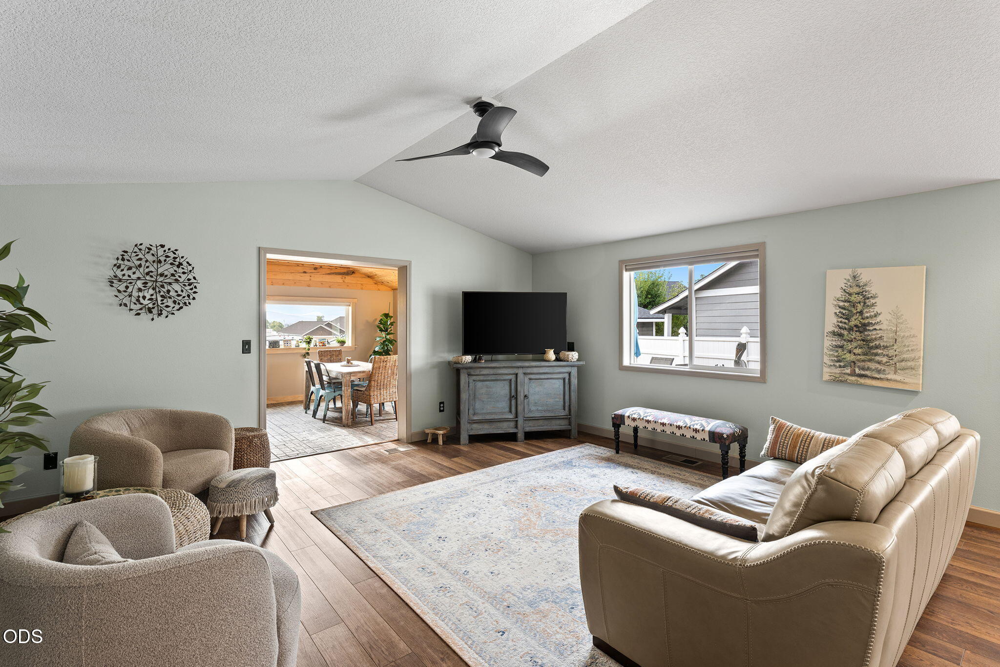 Living room with a beige leather sofa, pale rug, ceiling fan, and adjoining dining area.