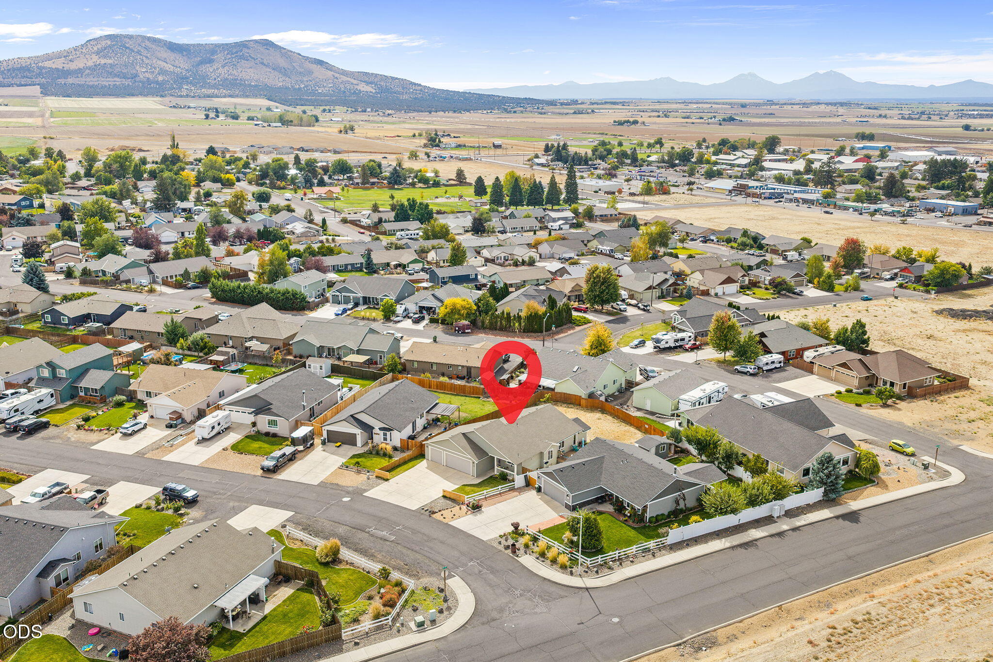 Aerial view of a residential neighborhood, with a red map pin marking a home and mountains in the distance.