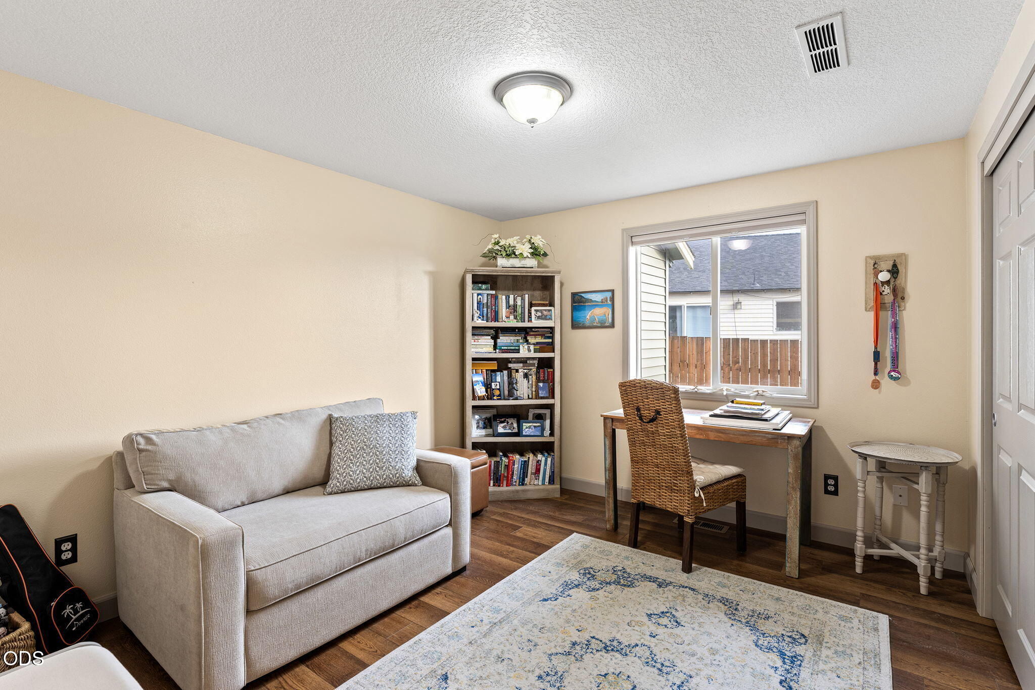 Home office with a gray loveseat, desk by the window, bookcase, and patterned rug.