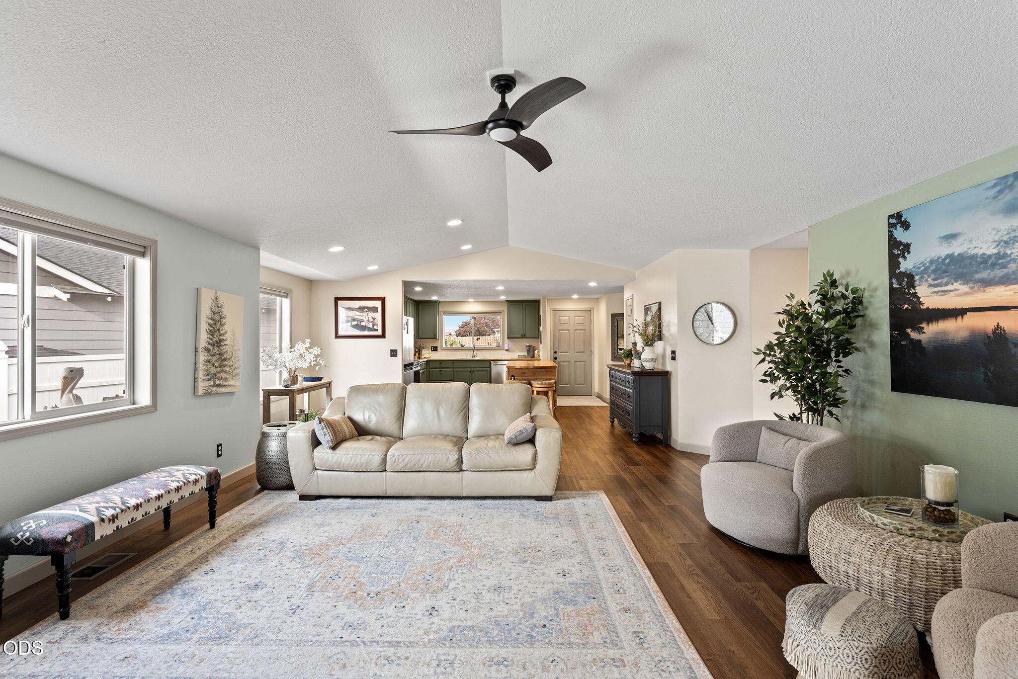 Open-plan living room with a white sofa, patterned rug, and green-cabinet kitchen beyond.