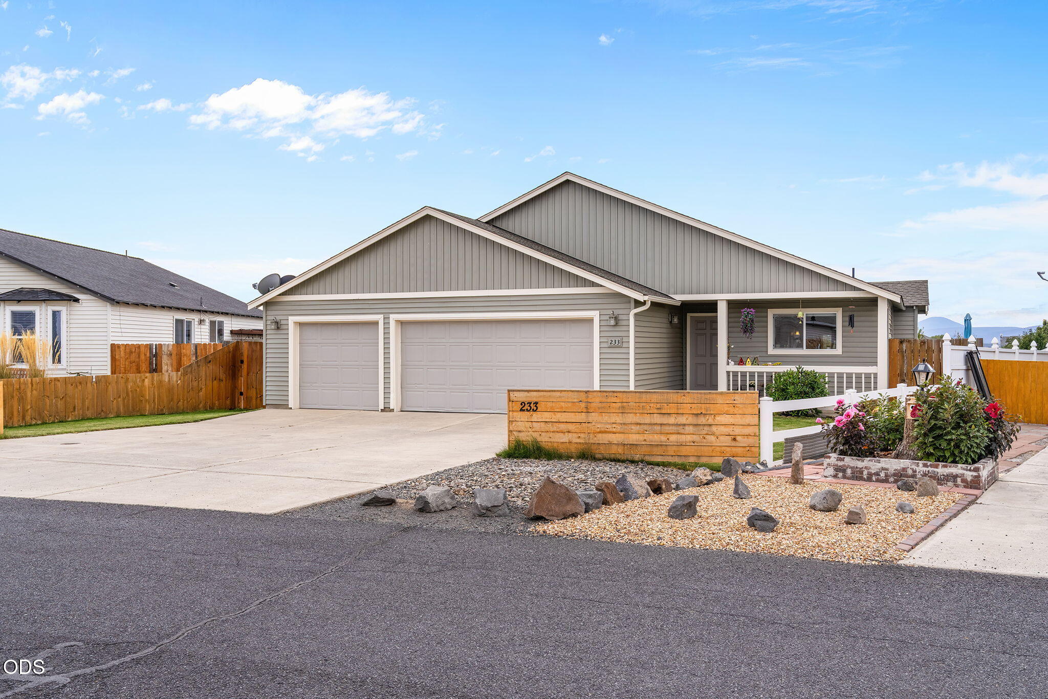 Gray single-story home with a double garage, covered porch, and gravel landscaping.