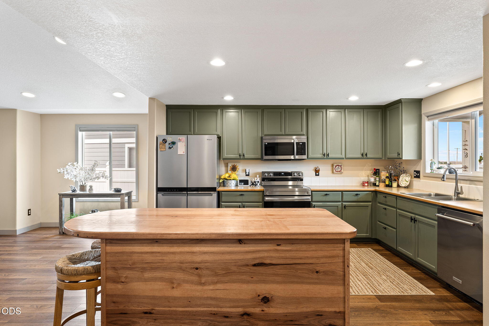 Kitchen with sage-green cabinets, stainless appliances, and a large natural-wood island.