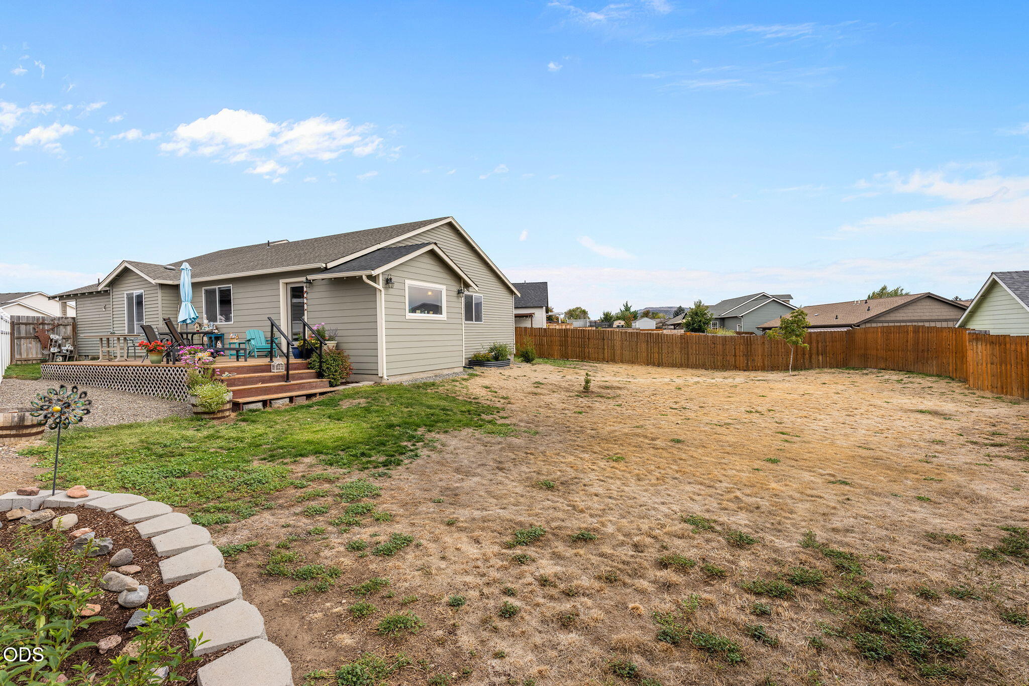 House rear and raised deck overlooking a fenced backyard with a broad dry lawn and curved stone path.