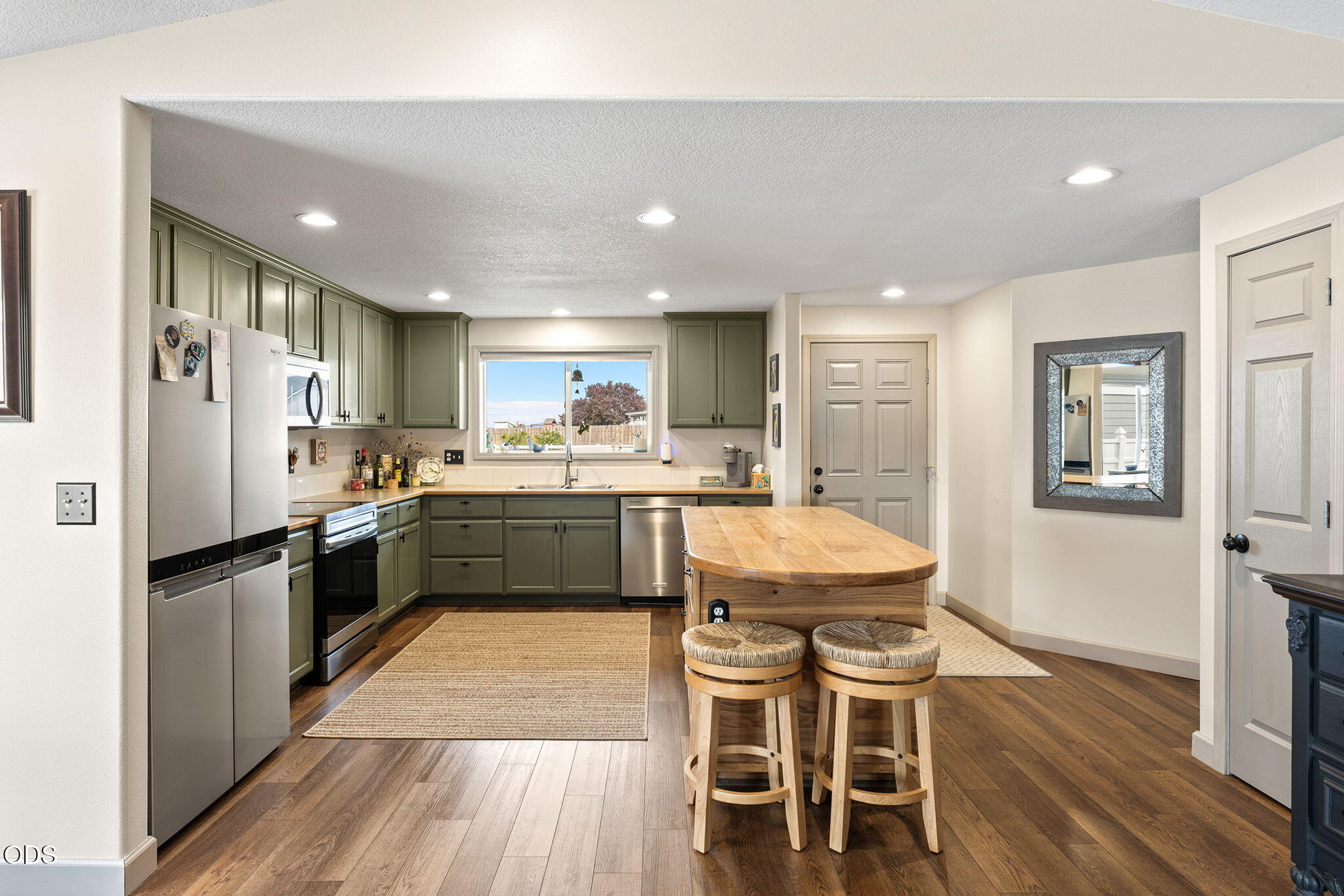 Kitchen with sage green cabinets, stainless appliances, and a butcher-block island with two stools.