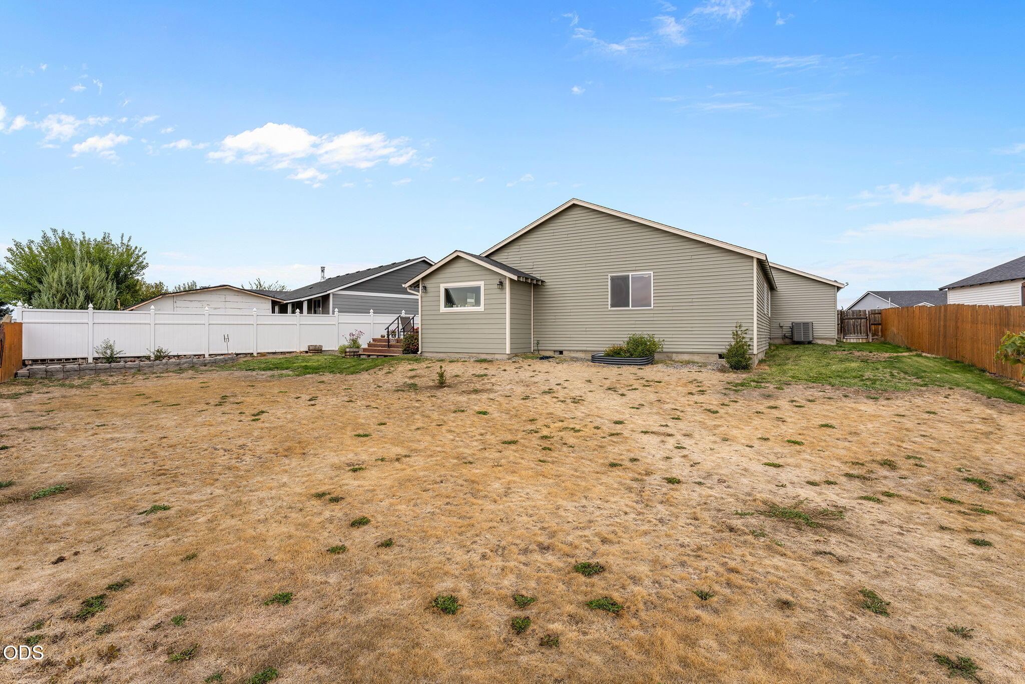 Home’s rear exterior with a wide dry lawn and fenced backyard.