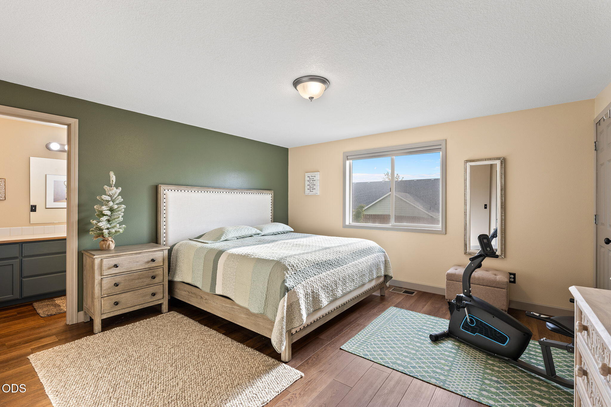 Bedroom with a green accent wall, large bed, and stationary exercise bike by the window.