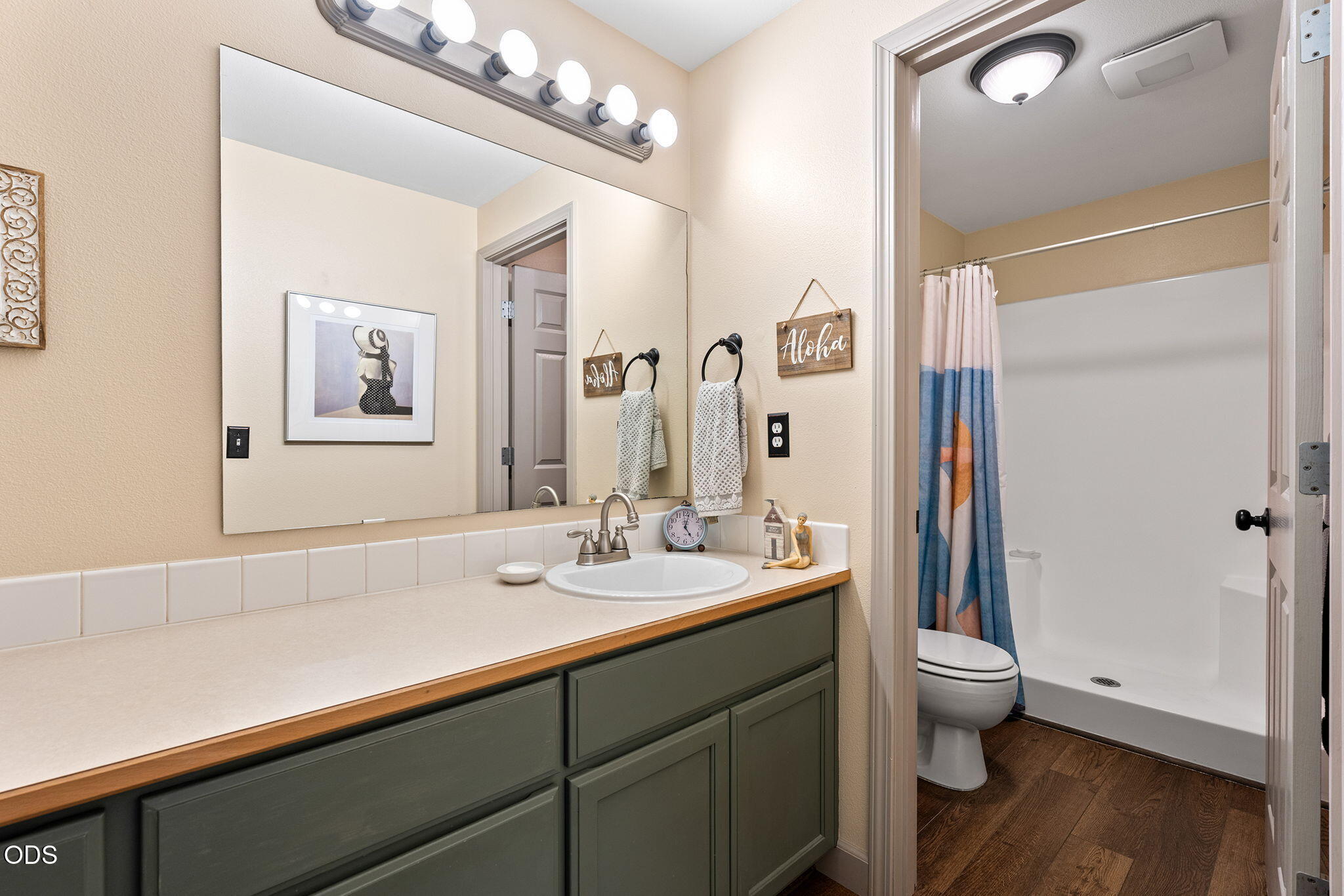 Bathroom with a long green vanity, broad mirror, and shower with a blue-and-pink curtain.
