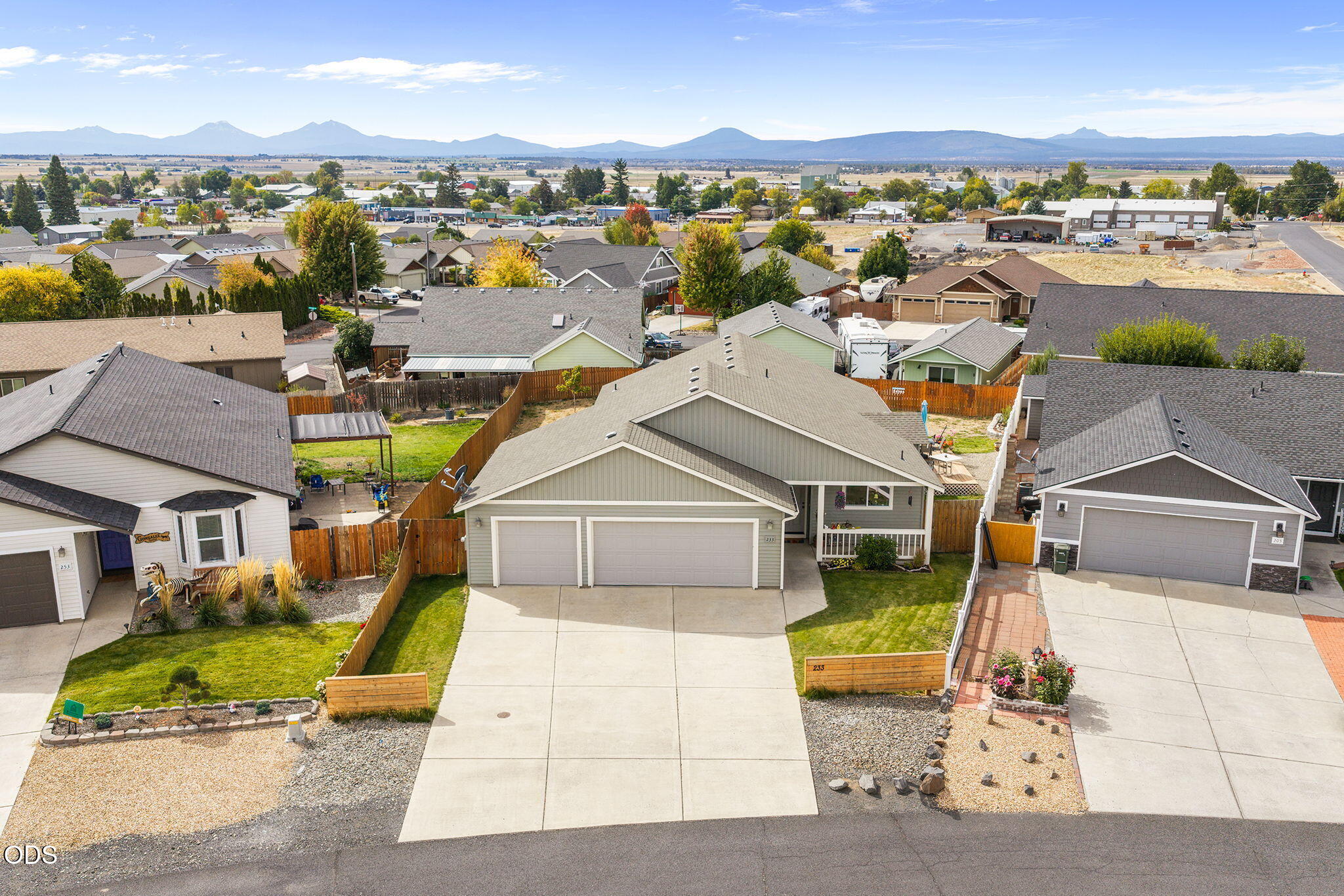 Aerial view of a single-story home with a double garage, fenced yard, and mountains on the horizon.