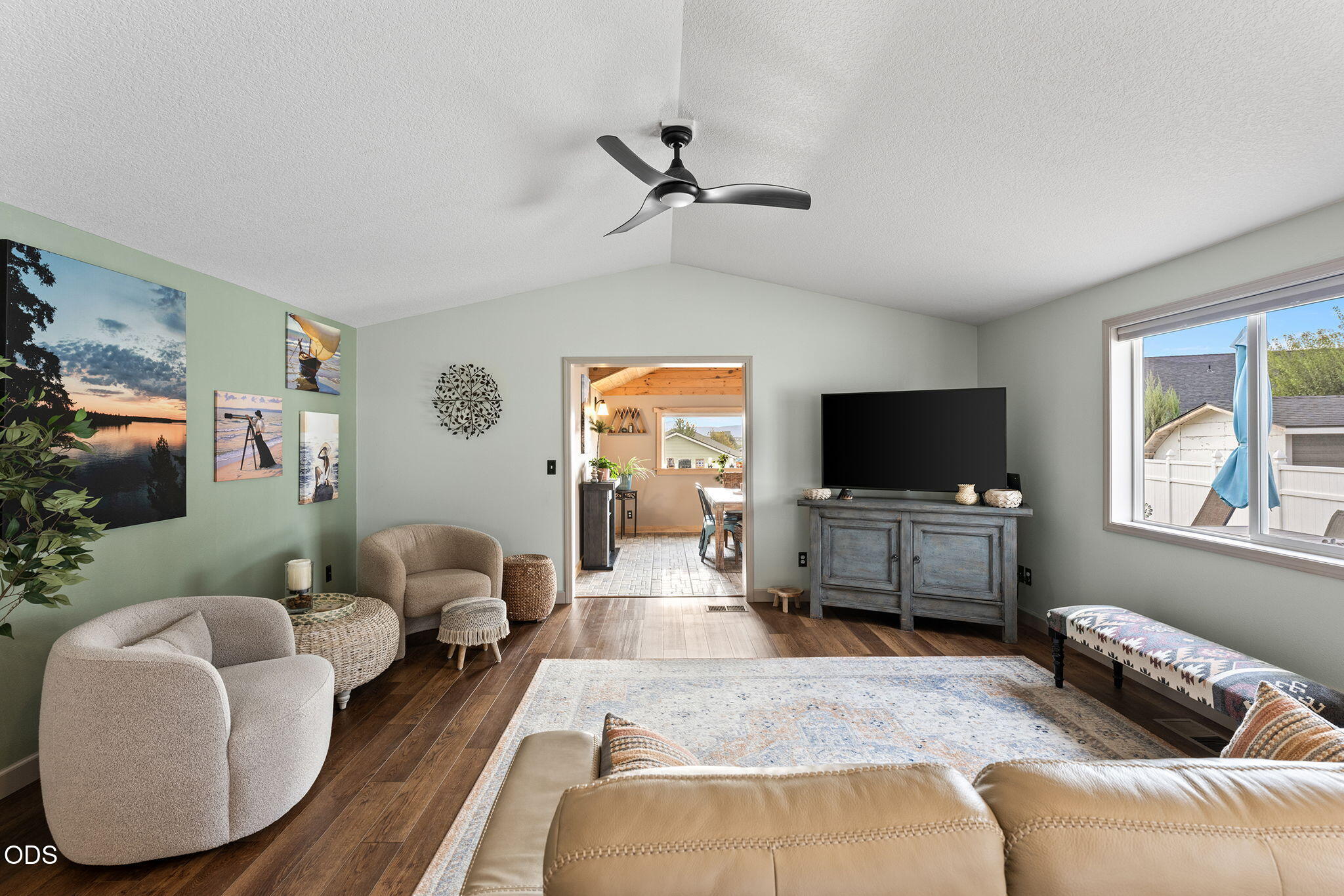 Furnished living room with cream seating, dark wood floors, a television, and a doorway to the dining area.