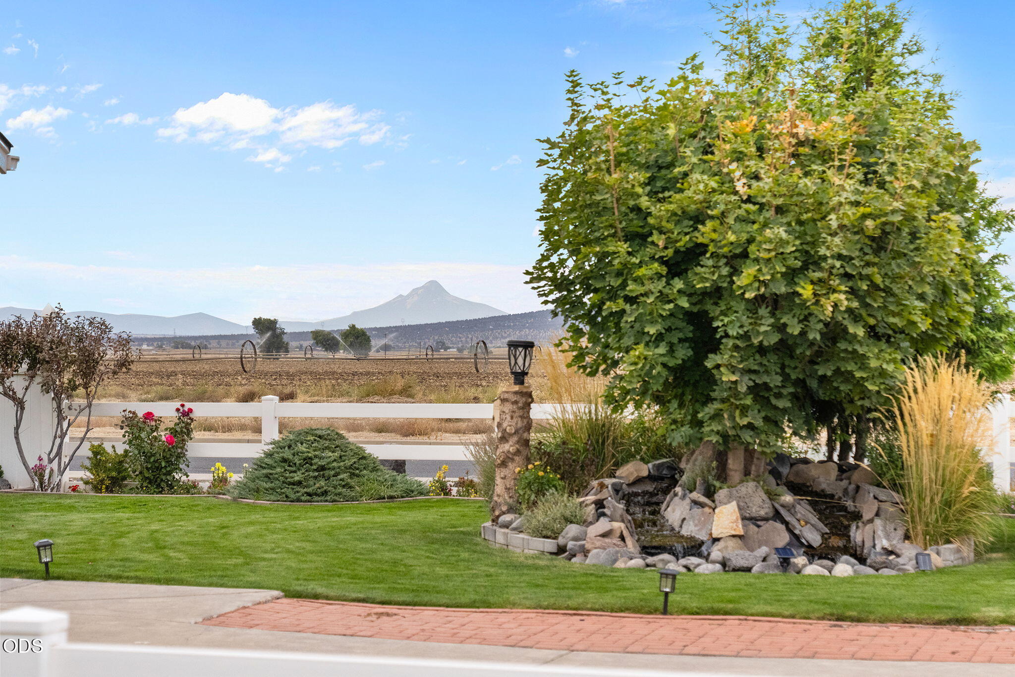 Landscaped yard with a rock water feature and mountain view beyond the white fence.