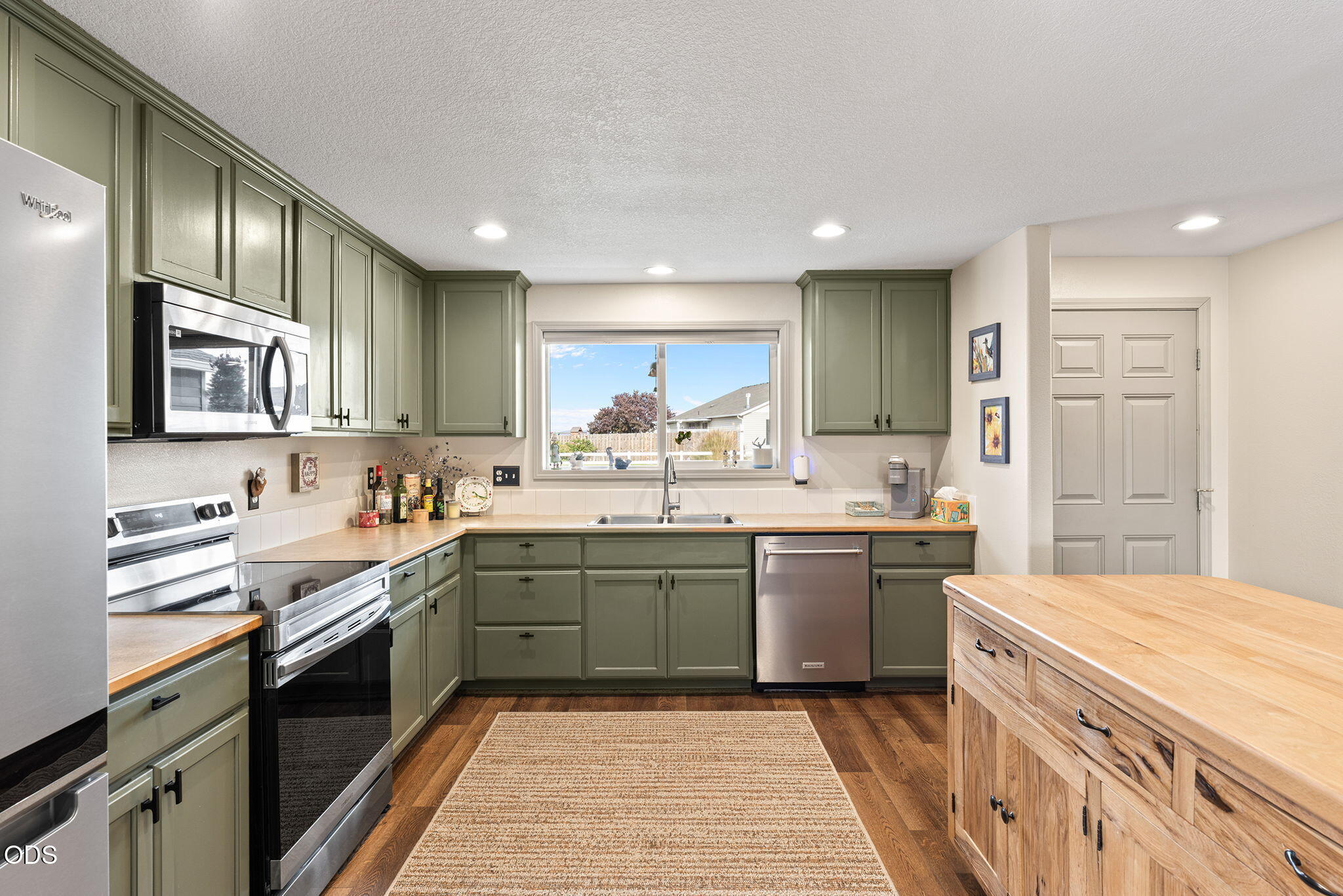 Kitchen with sage green cabinets, stainless steel appliances, and a wooden island.