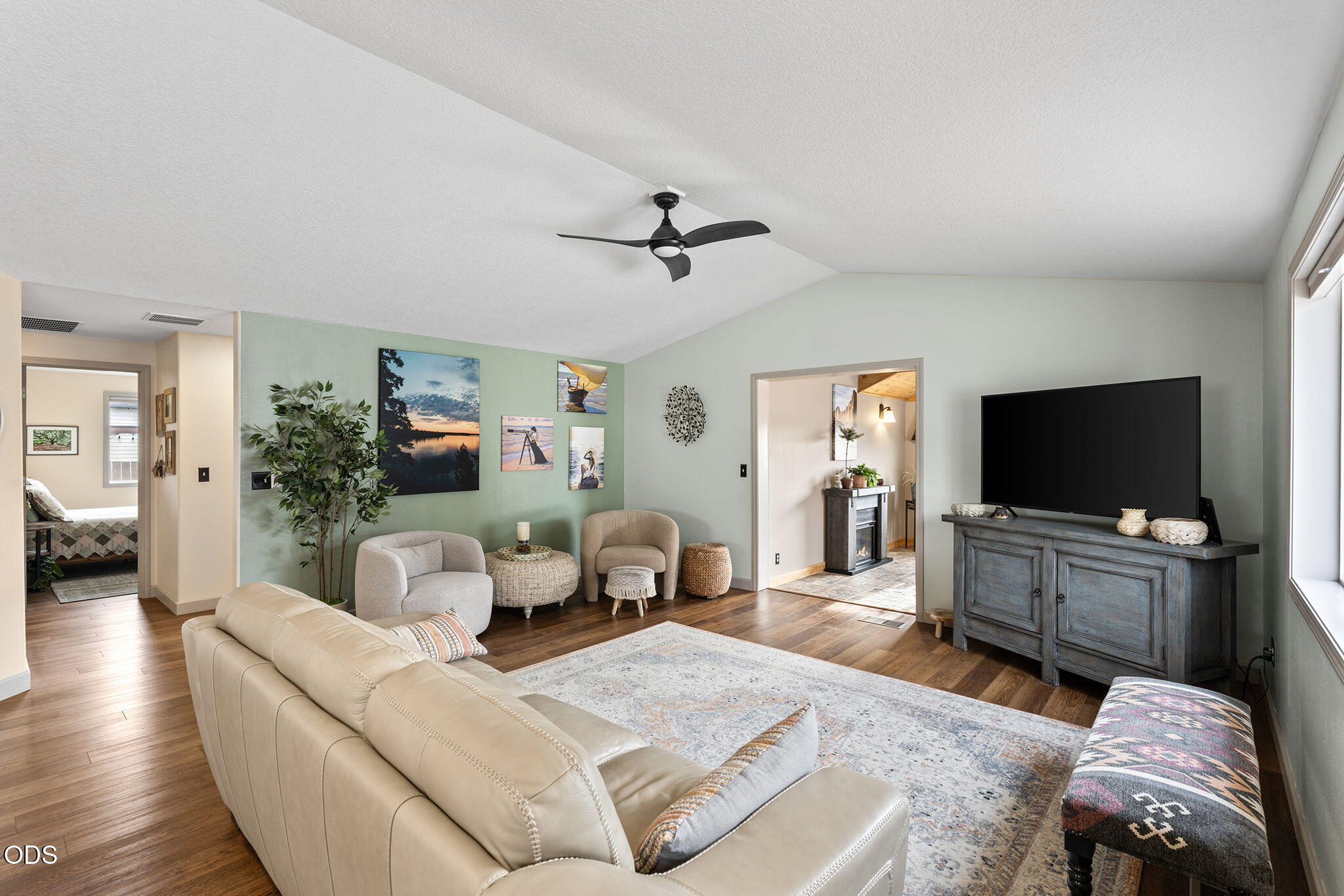 Living room with vaulted ceiling, pale green accent wall, beige seating, and large TV.