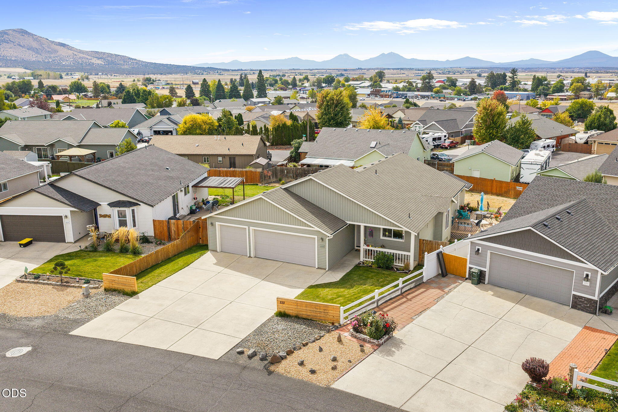 Aerial view of a single-story home with a two-car garage, fenced yard, and mountains beyond the neighborhood.