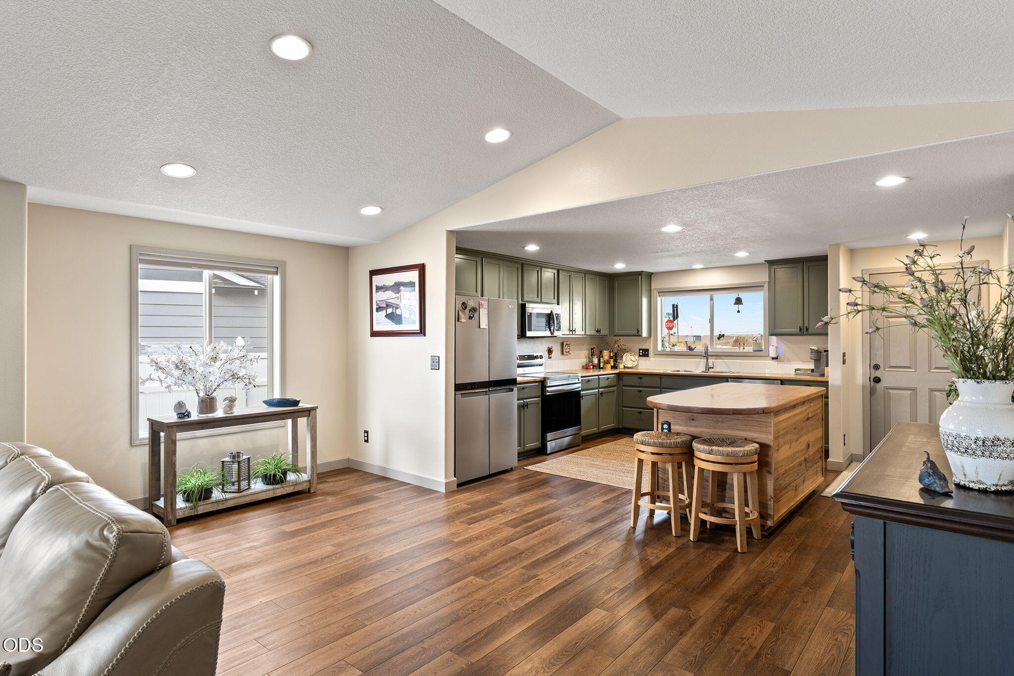 Open-plan kitchen with green cabinets, stainless steel appliances, and a wood island with stools.