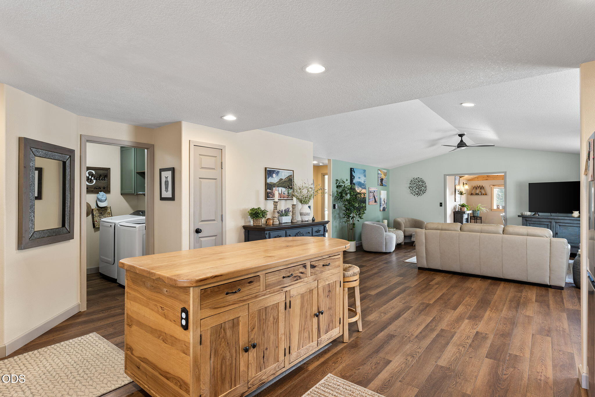 Open-plan living room with a wooden island, beige sectional, dark wood floors, and laundry nook.