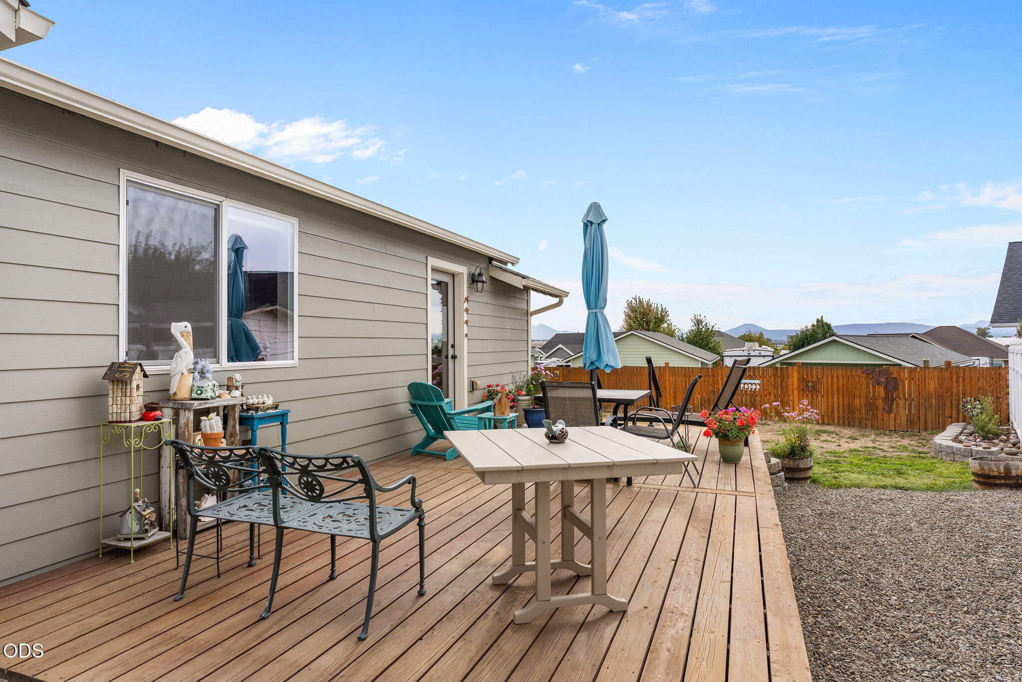Furnished wooden deck with outdoor dining areas, flower planters, and distant mountain views.
