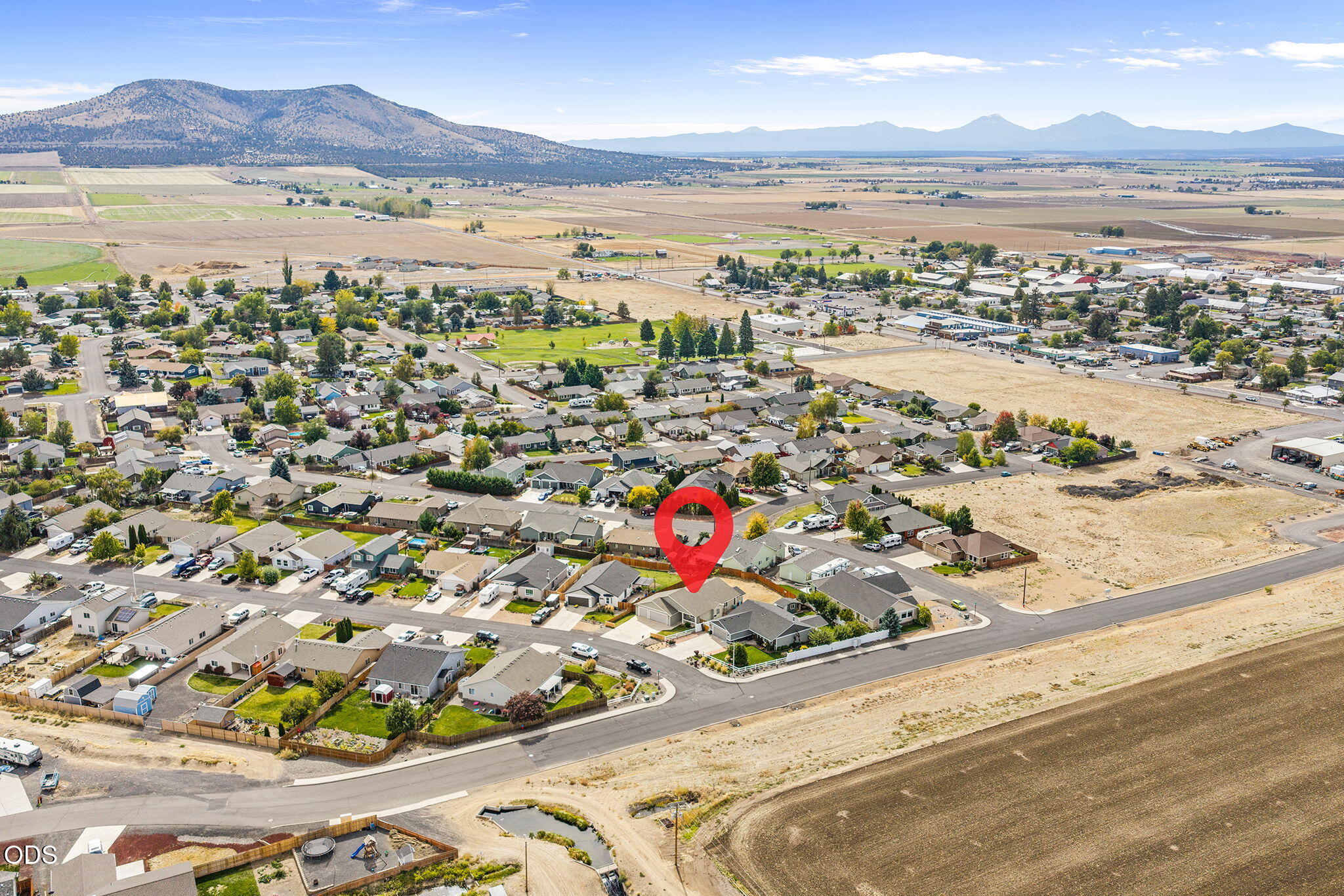 Aerial view of a residential neighborhood with the marked home, open fields, and distant mountains.