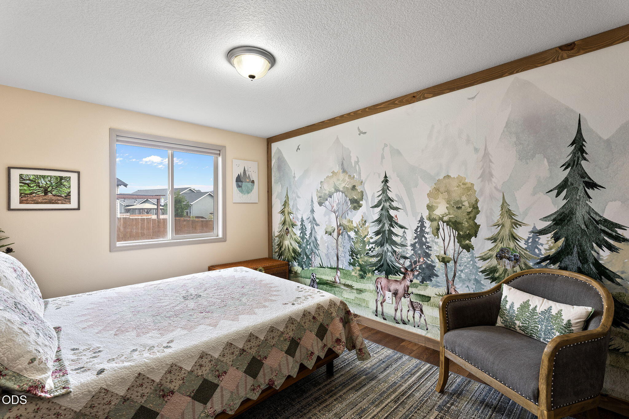 Bedroom with a patchwork quilt bed and a woodland mural of trees and deer.