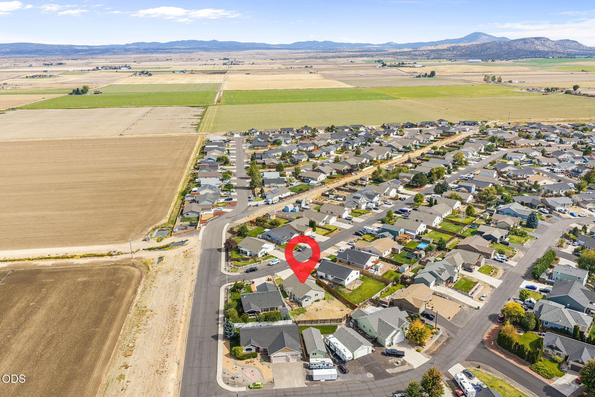 Aerial view of a neighborhood beside farmland, with a red marker identifying the property.