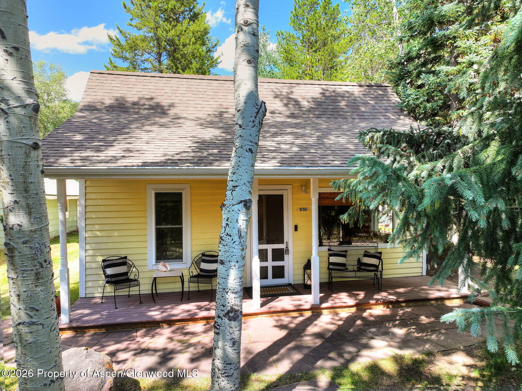 Yellow house with a covered, furnished porch framed by aspen trees.