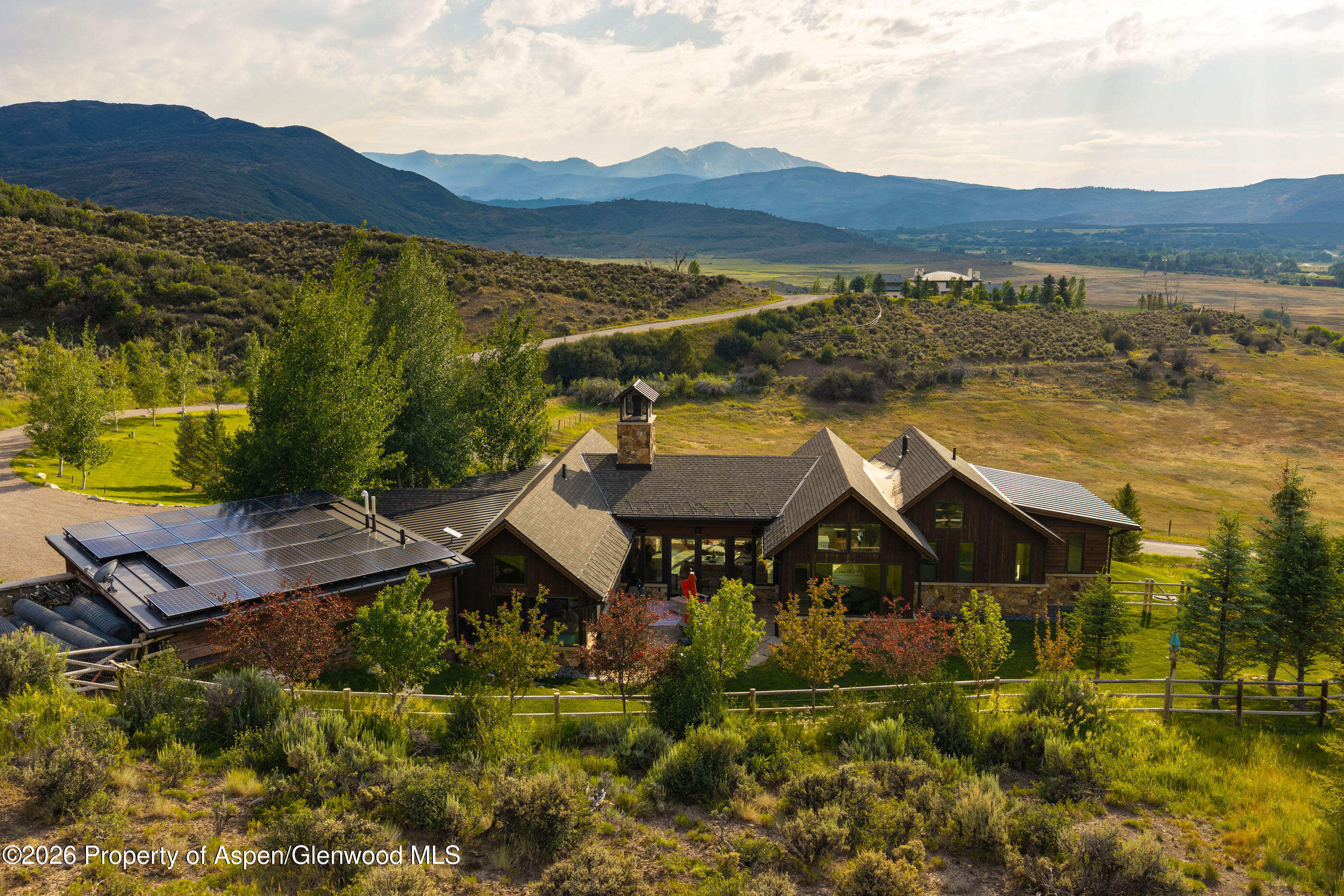 Timber-and-stone mountain home with rooftop solar panels and distant mountain views.