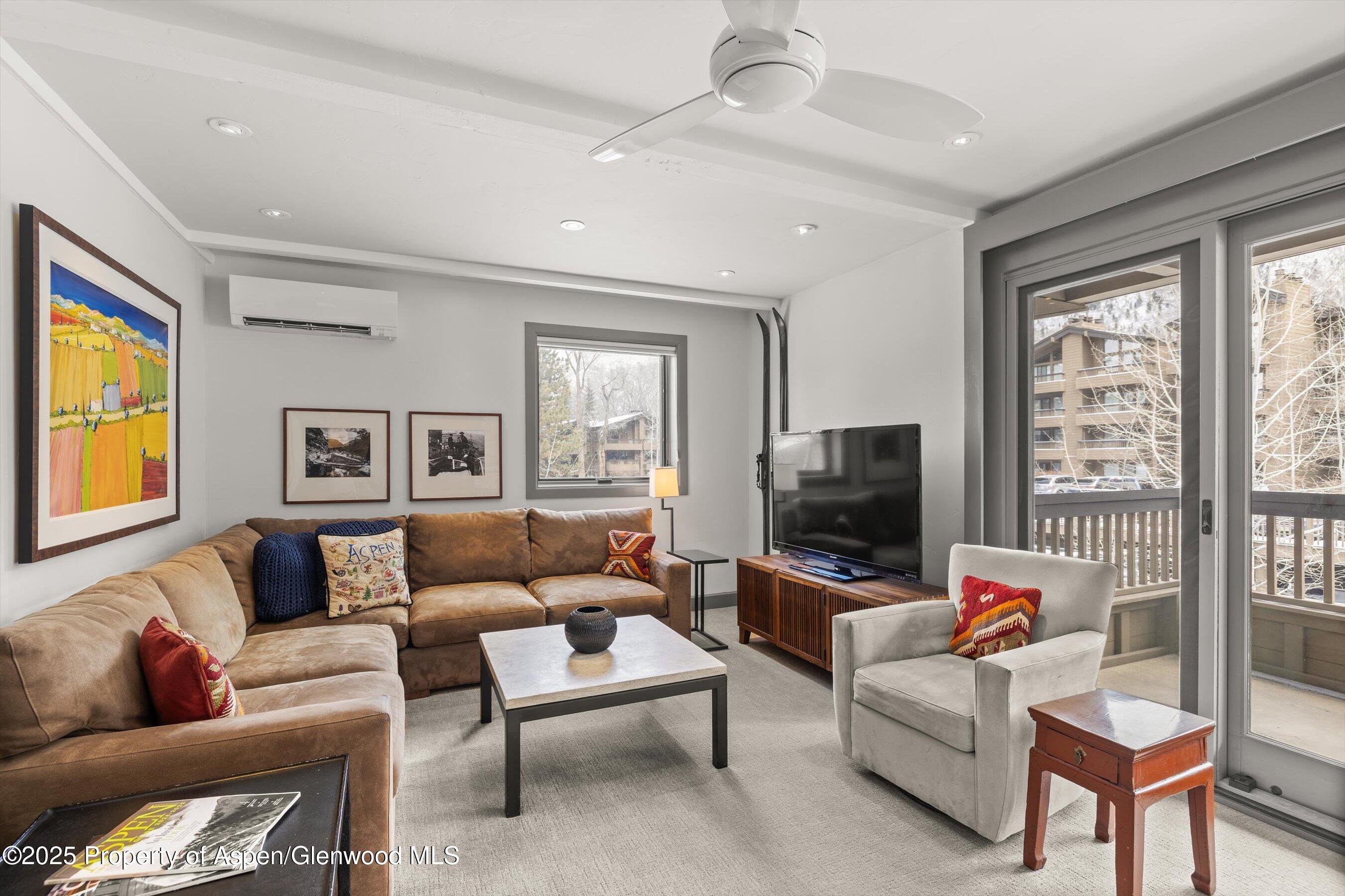 Furnished living room with a brown sectional, white armchair, and glass doors to a balcony.