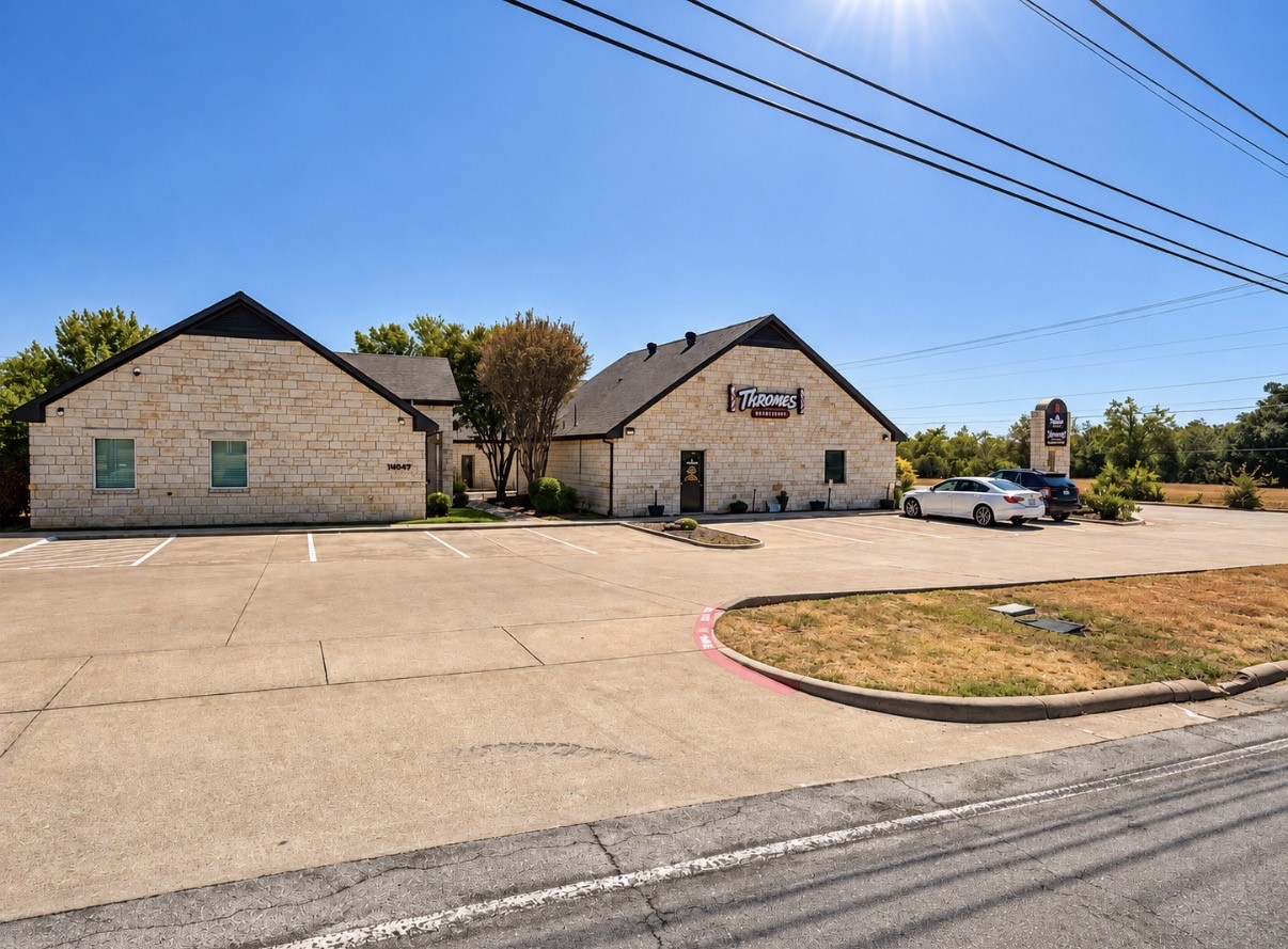Stone commercial building with dark gabled roofs, business sign, and a wide parking lot.