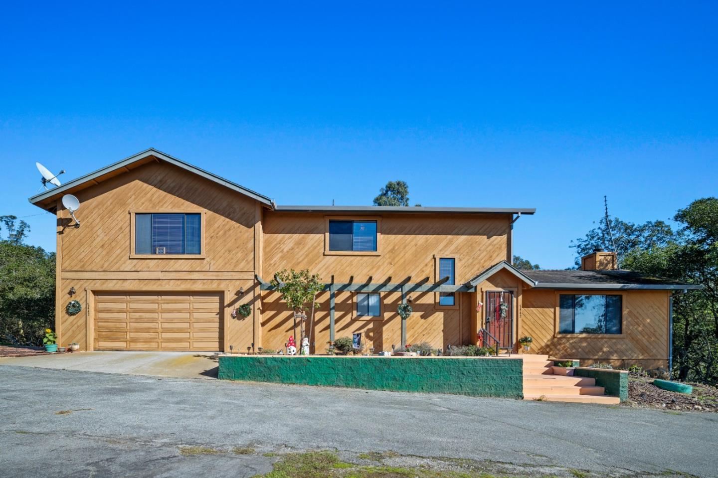 Two-story wood-sided home with an attached garage, entry pergola, and broad paved driveway.