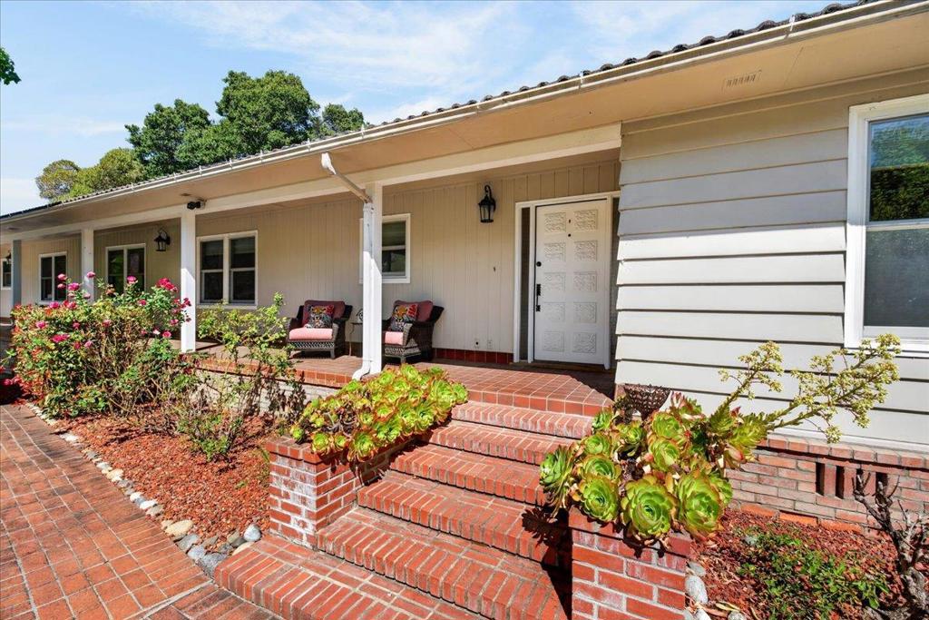 Single-story home with a covered porch, brick steps, and landscaped beds of roses and succulents.