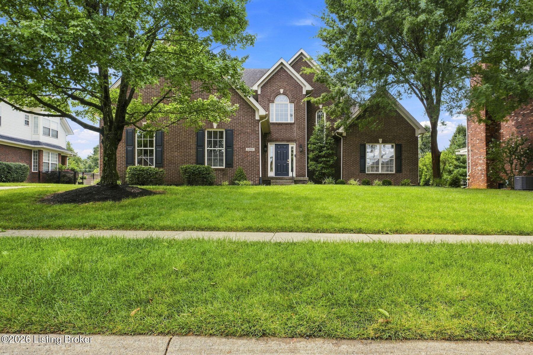 Brick two-story home with a blue front door, mature shade trees, and a broad green lawn.