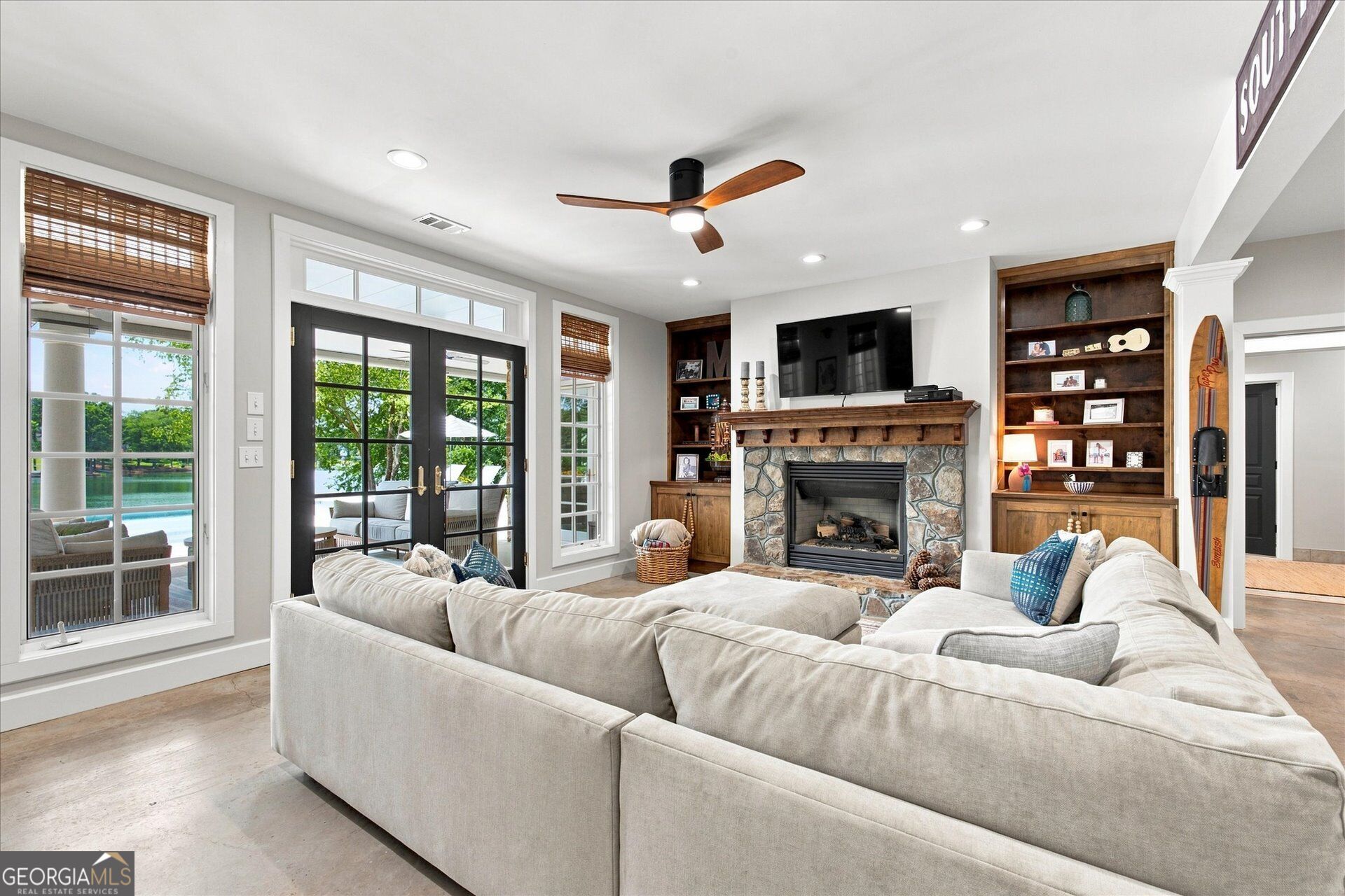 Living room with a stone fireplace, built-in shelves, and windows overlooking a pool and lake.