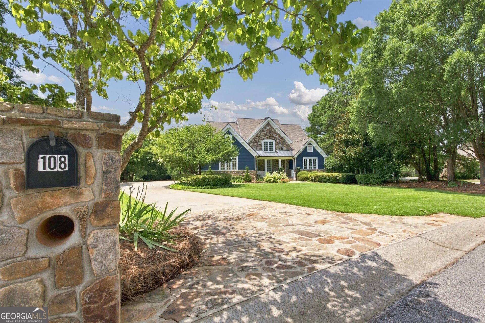 Blue home with stone facade, landscaped lawn, stone-paved driveway, and a stone mailbox marked 108.