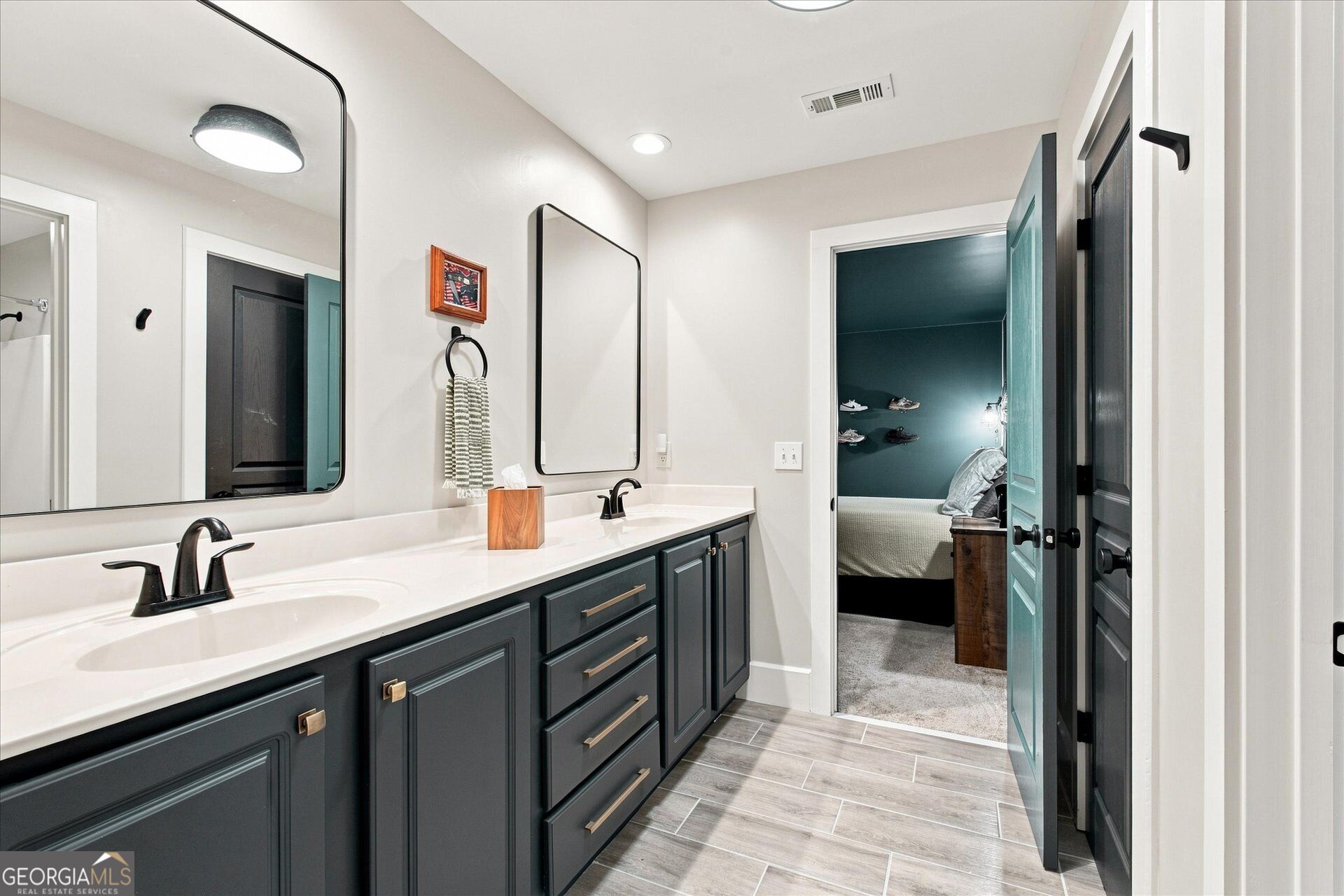 Bathroom with a double-sink vanity, charcoal cabinets, and an open teal door to a bedroom.