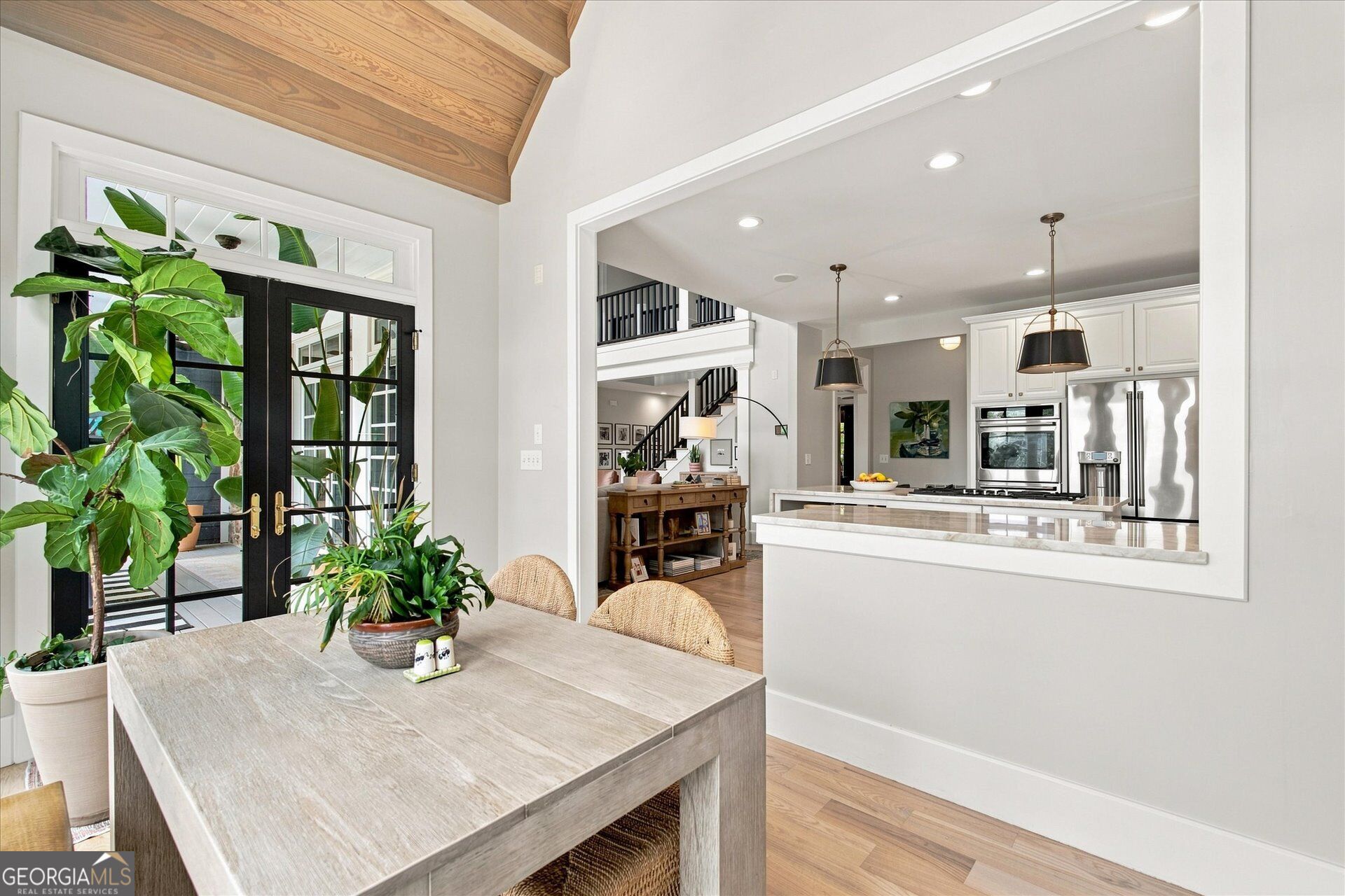 Dining area opening to a white kitchen, with a vaulted wood ceiling and black-framed glass doors.