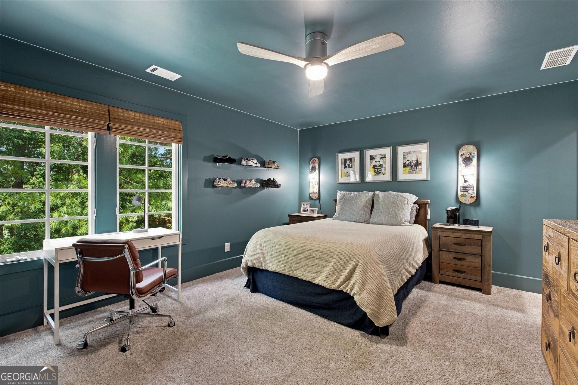 Bedroom with teal walls, a large bed, desk by bright windows, and shoes displayed on floating shelves.