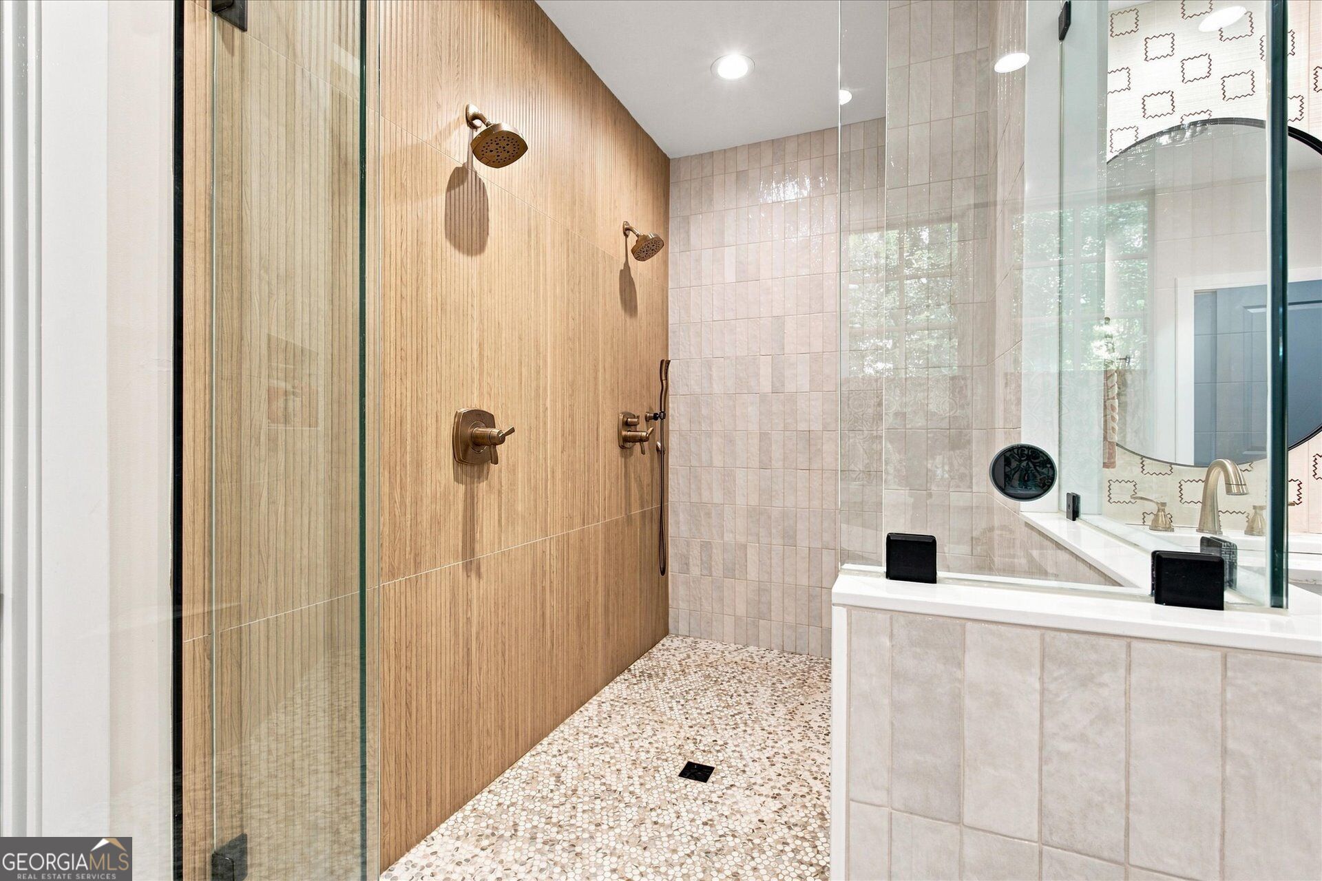 Bathroom with a glass-enclosed double-head shower, wood-look tile wall, pebble floor, and built-in tub.