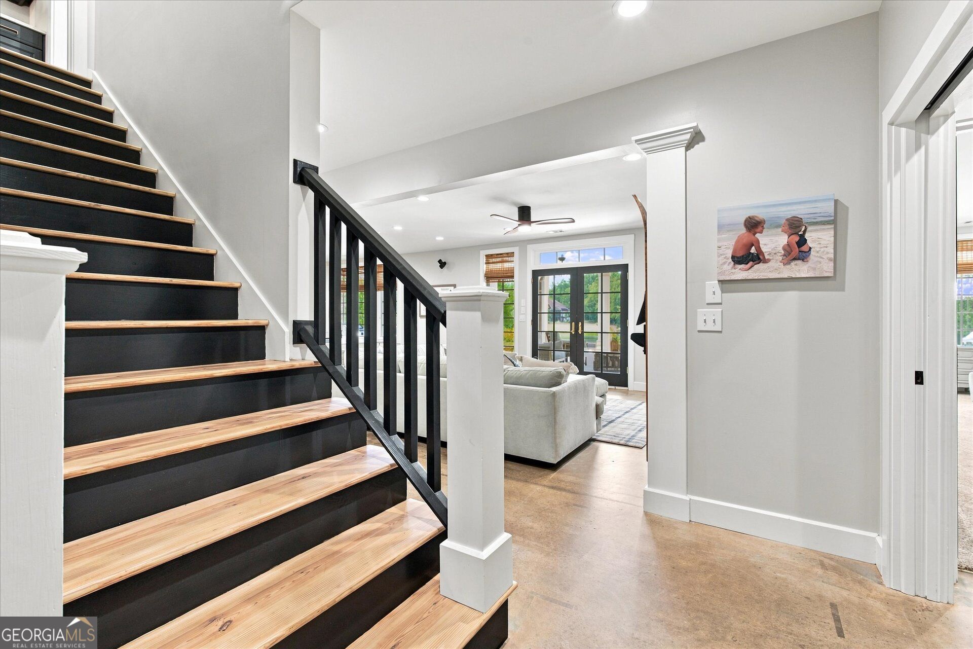 Interior staircase with black risers and railing, natural wood treads, and a view into the living room.