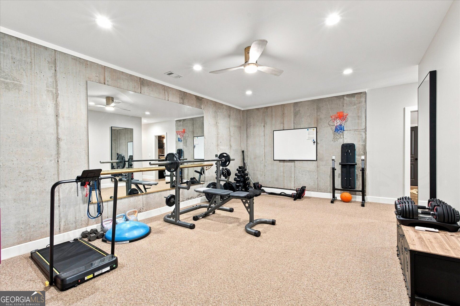 Home gym with a mirrored concrete wall, treadmill, weight benches, and dumbbells.