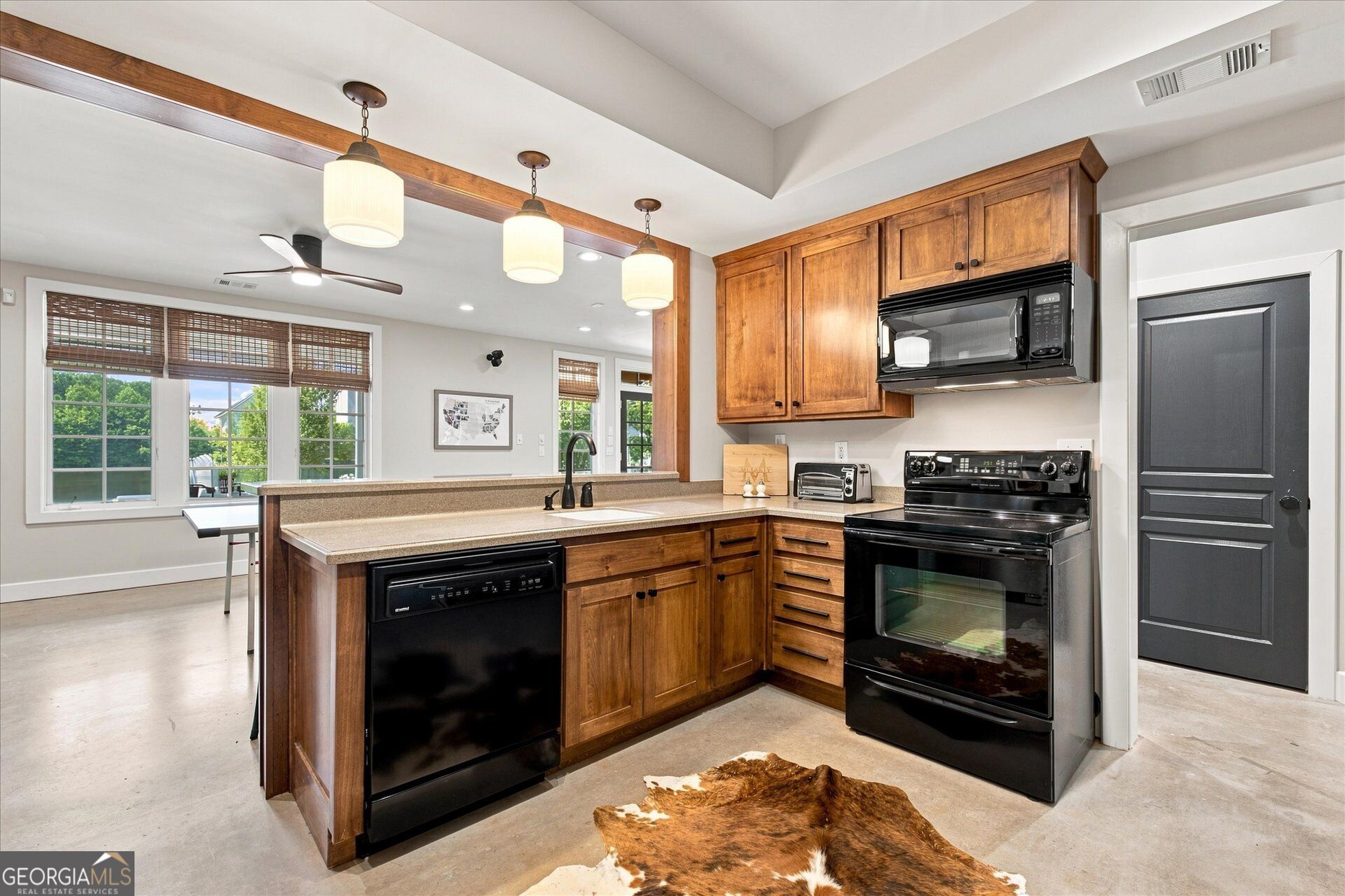 Kitchen with warm wood cabinetry, a large island, and black appliances beside a bright dining area.