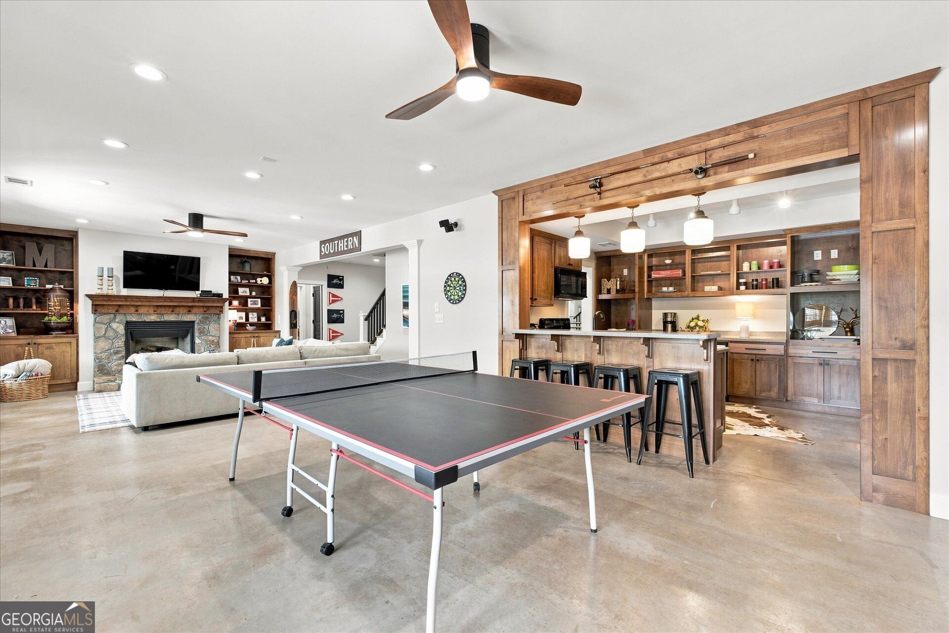 Open recreation room with a ping-pong table, stone fireplace, sofa, and wood-paneled bar.