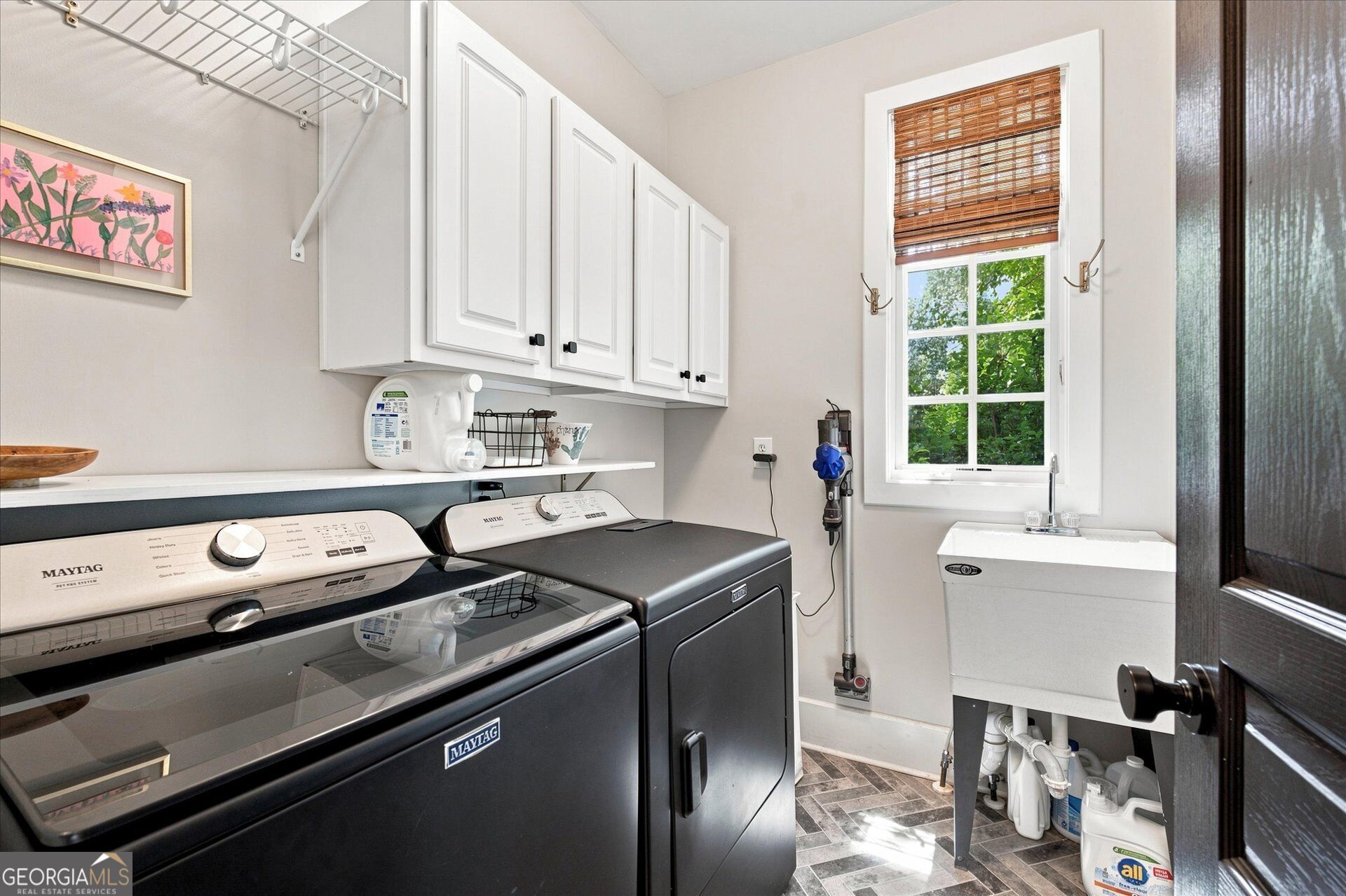 Laundry room with Maytag washer and dryer, white cabinets, and a utility sink by the window.