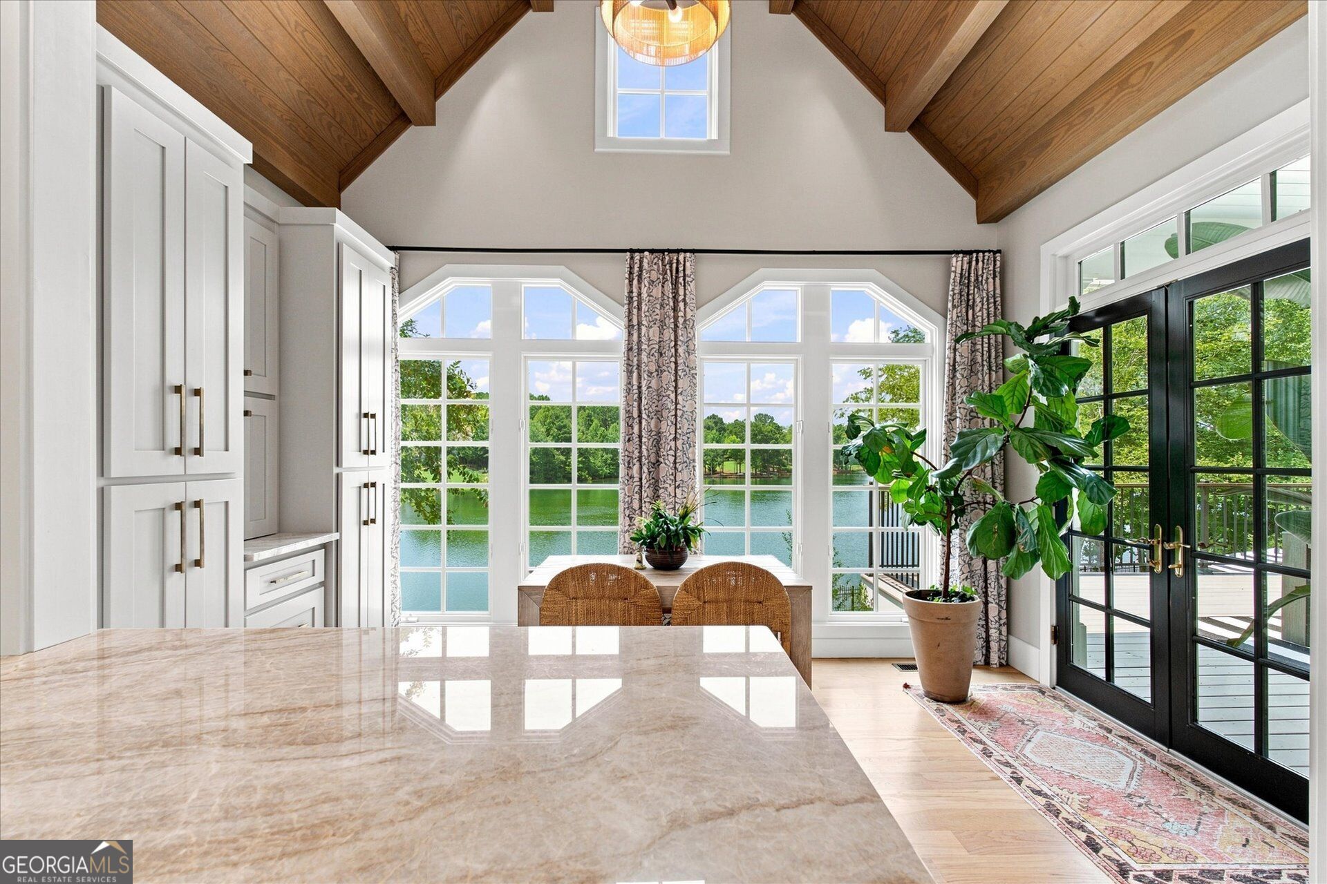 Bright kitchen with a vaulted wood ceiling, lake-view windows, and black French doors.