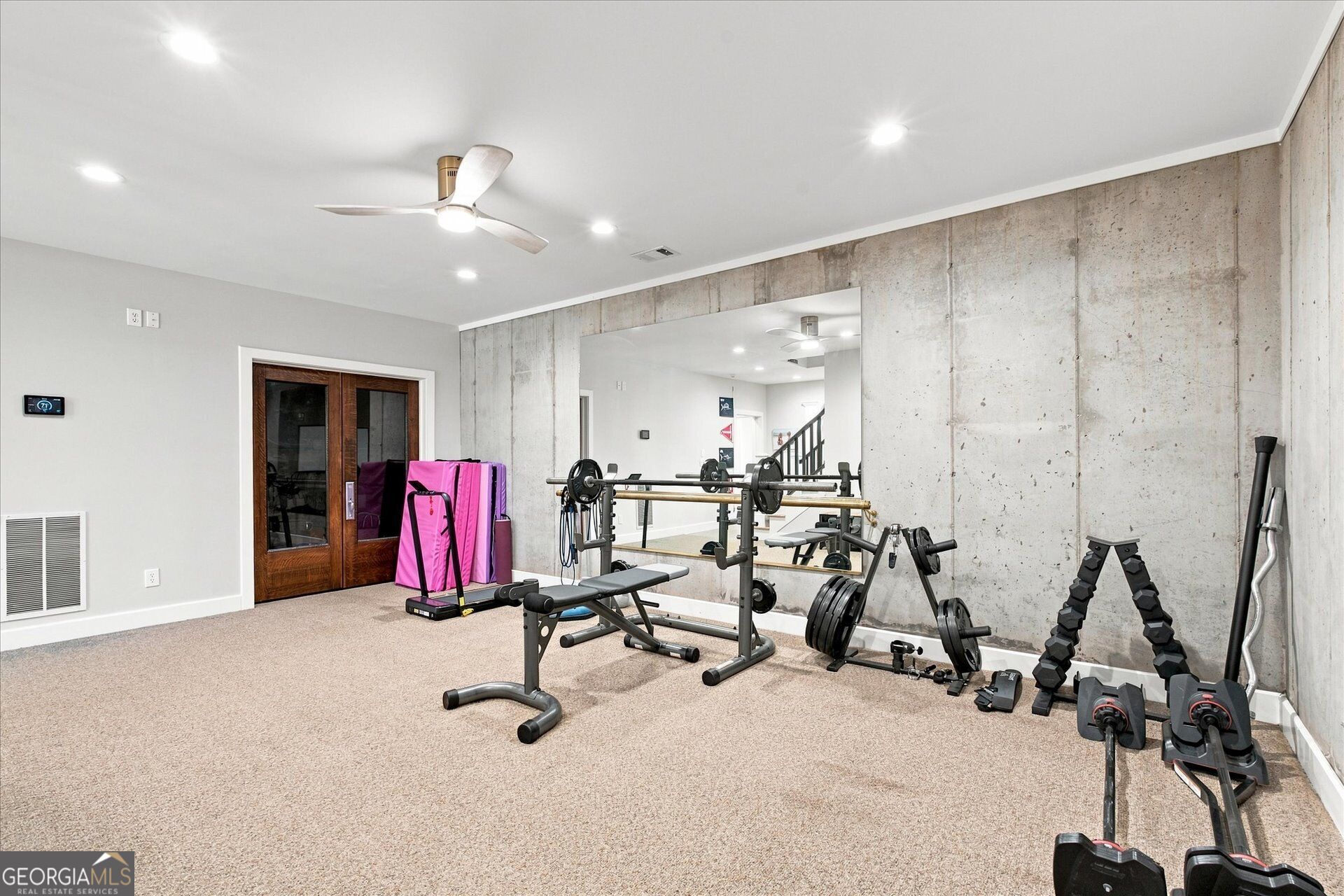 Home gym with a squat rack, weight bench, dumbbells, and a large mirror against an exposed concrete wall.