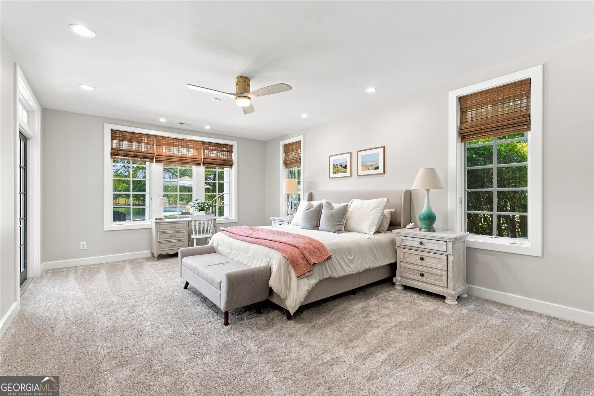 Bright bedroom with a large bed, woven window shades, and a pool visible outside.
