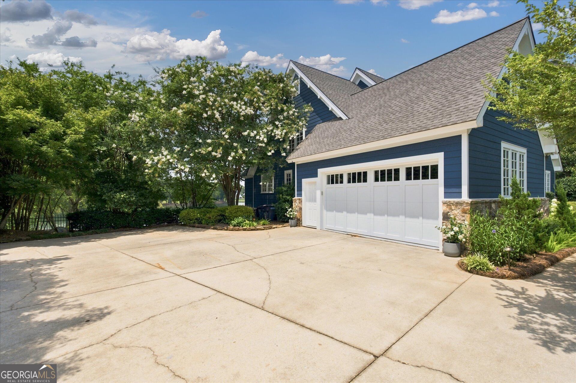 Blue-sided home with a white double garage door, stone base, and broad concrete driveway.