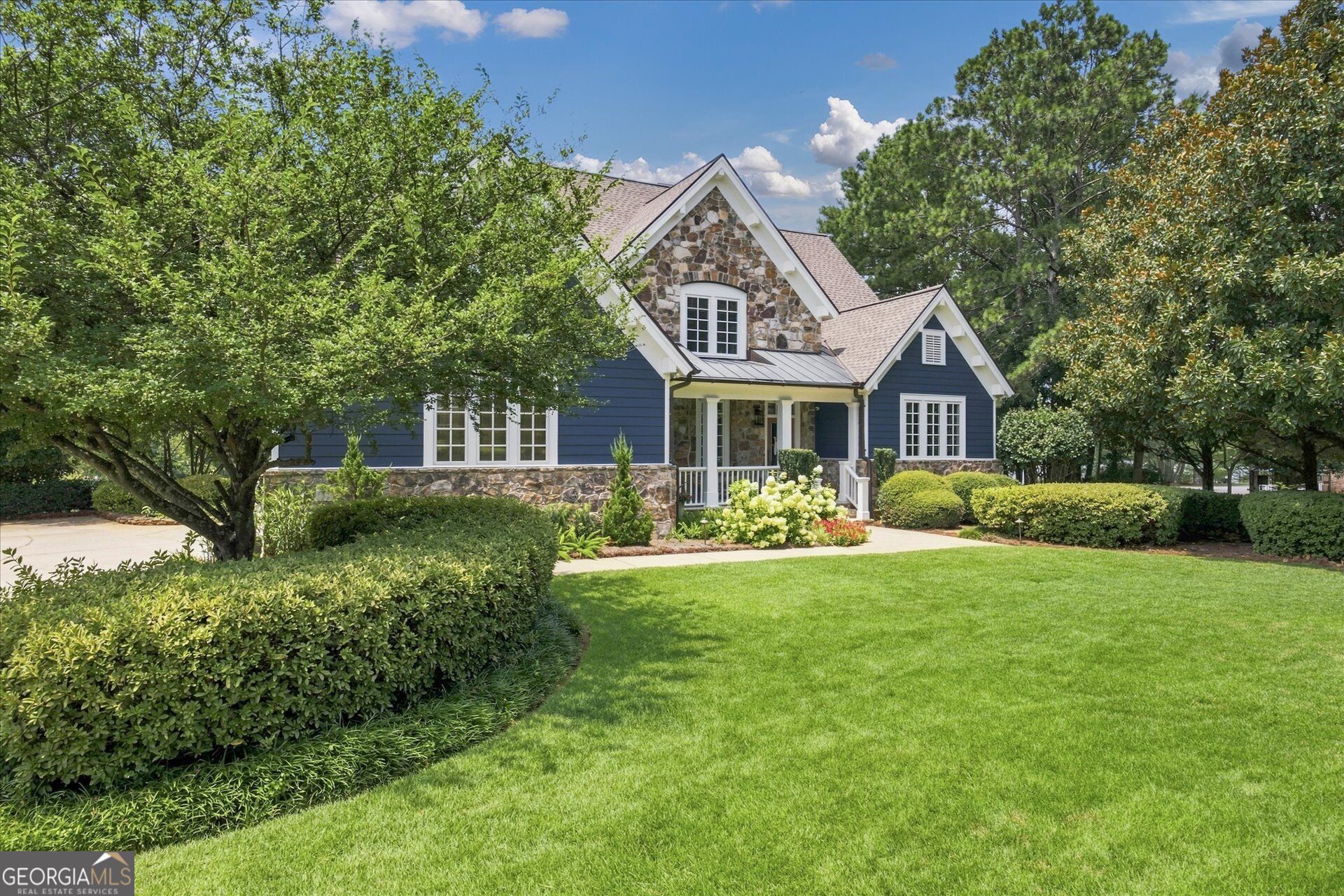 Blue house with stone accents and a covered porch, framed by mature trees and a landscaped lawn.