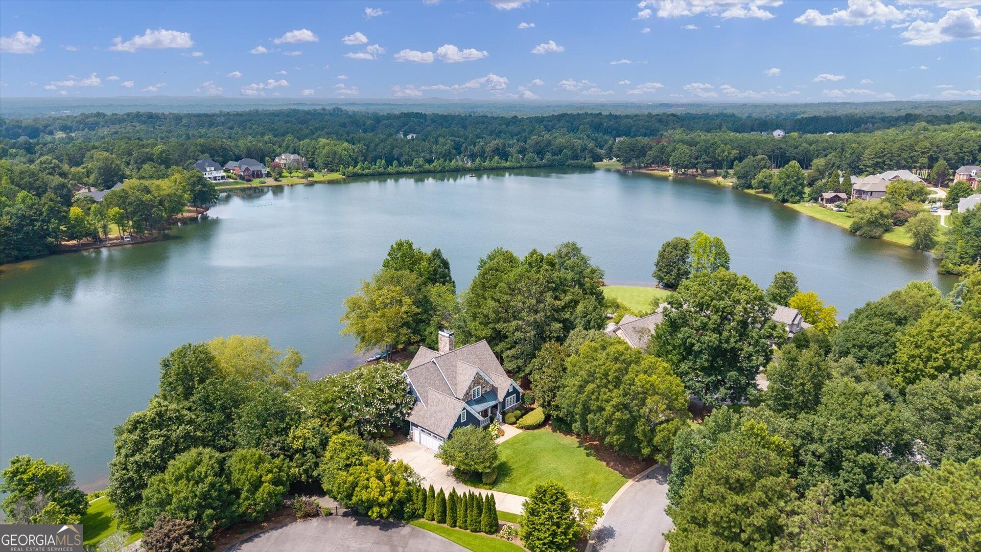 Aerial view of a lakeside home with wooded grounds and broad water views.