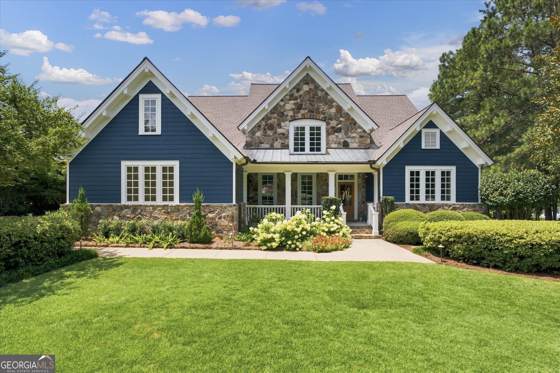 Blue house with stone accents, covered porch, and landscaped front lawn.